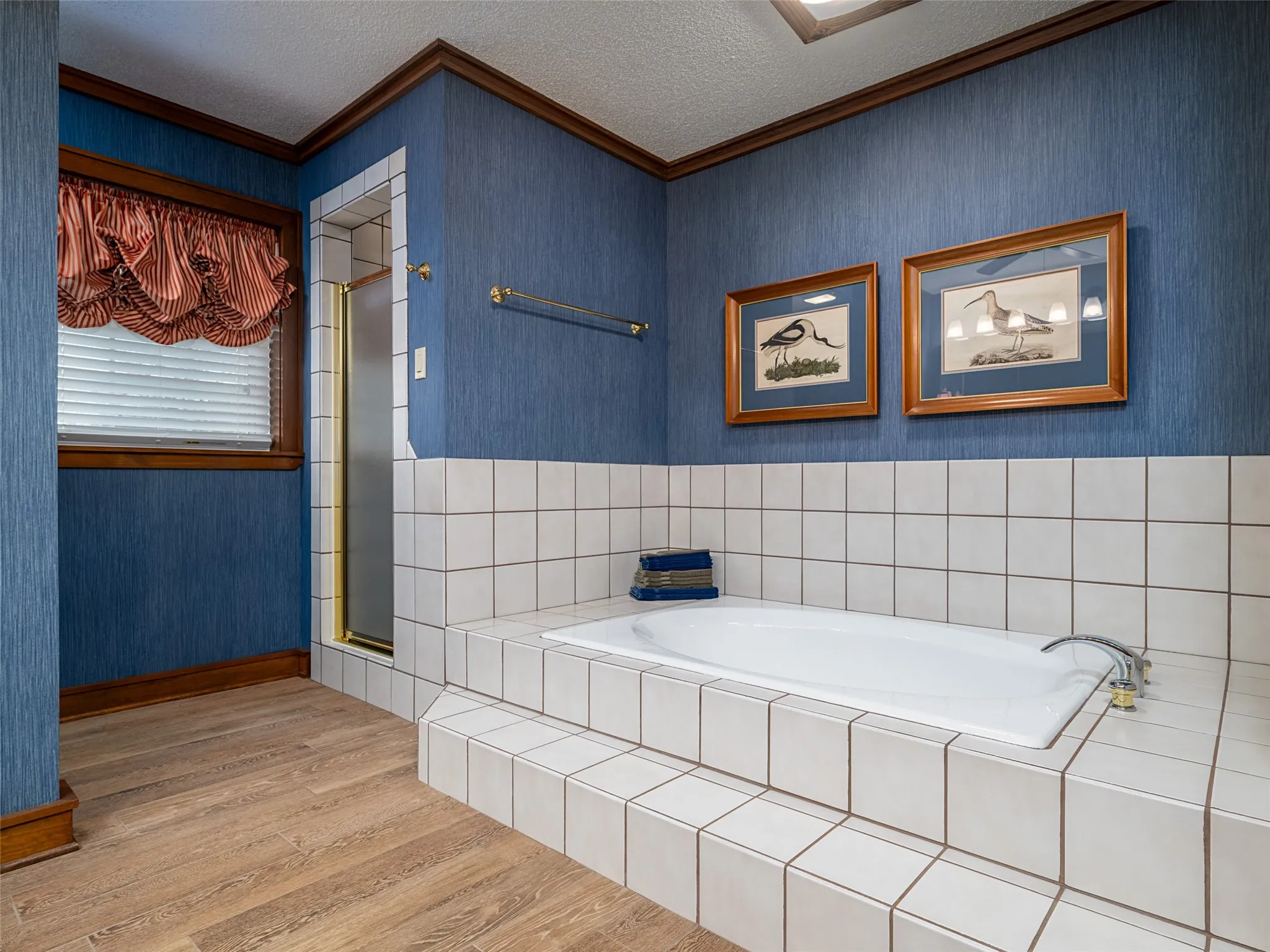 White tile surround with a built-in soaking tub, wood-finish flooring, and a glass-enclosed shower