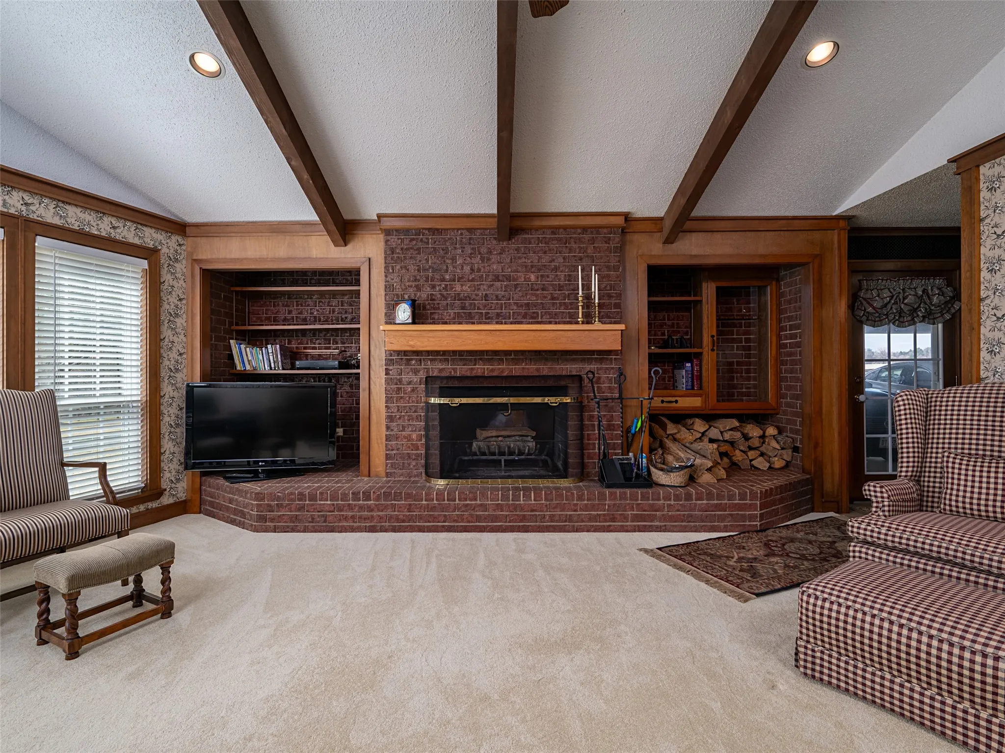 Brick fireplace with hearth, built-in shelving, vaulted ceiling with exposed beams, and recessed lighting