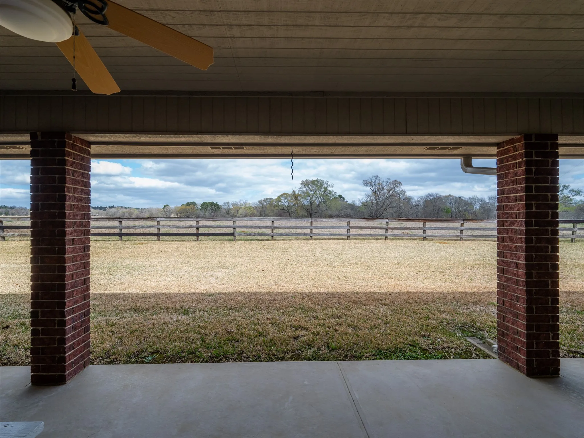 Covered patio with brick columns, concrete flooring, and a ceiling fan