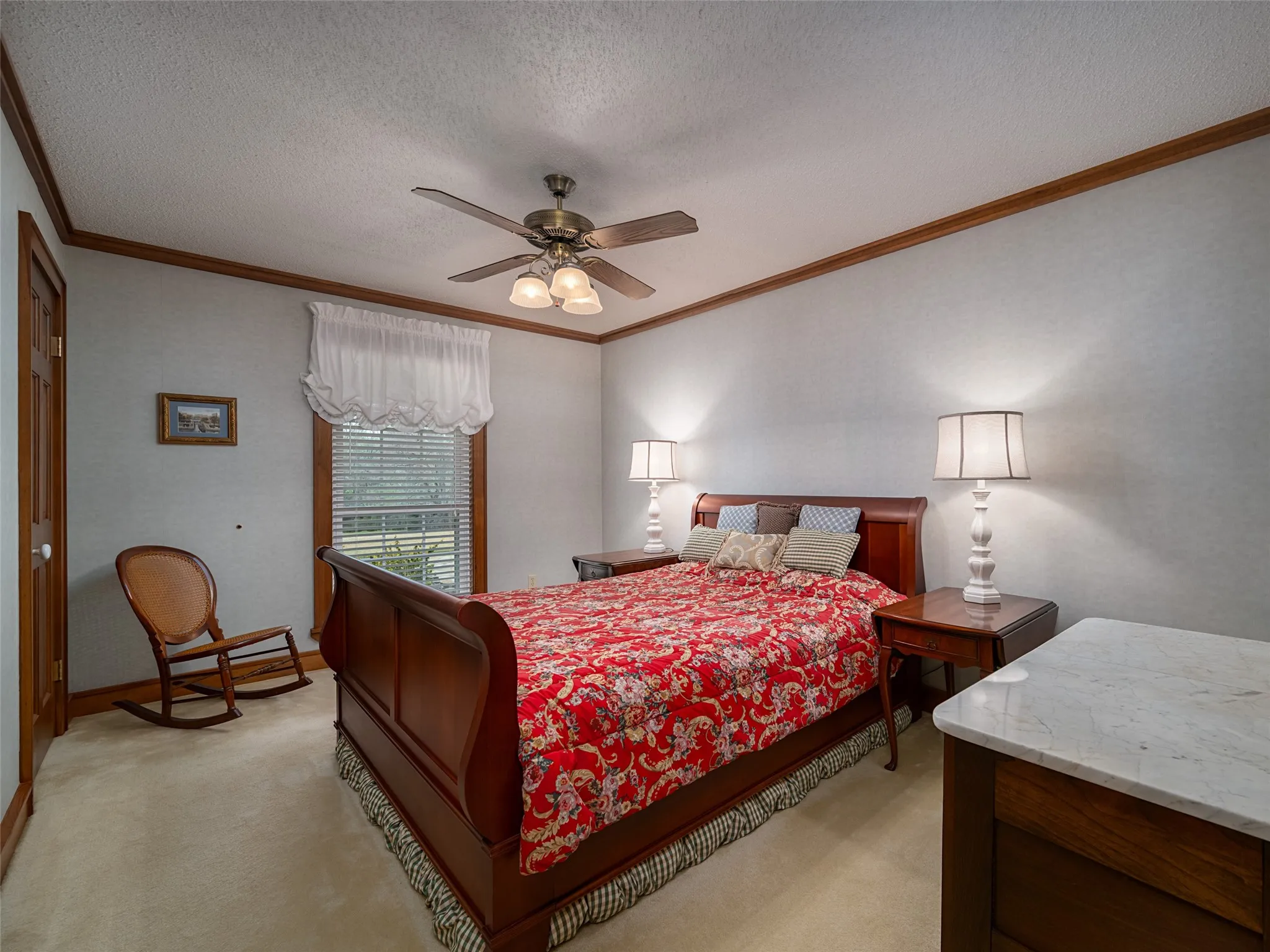 Textured wall finish, wood-trimmed doorway, wood-framed window with blinds, ceiling fan, and carpeted flooring