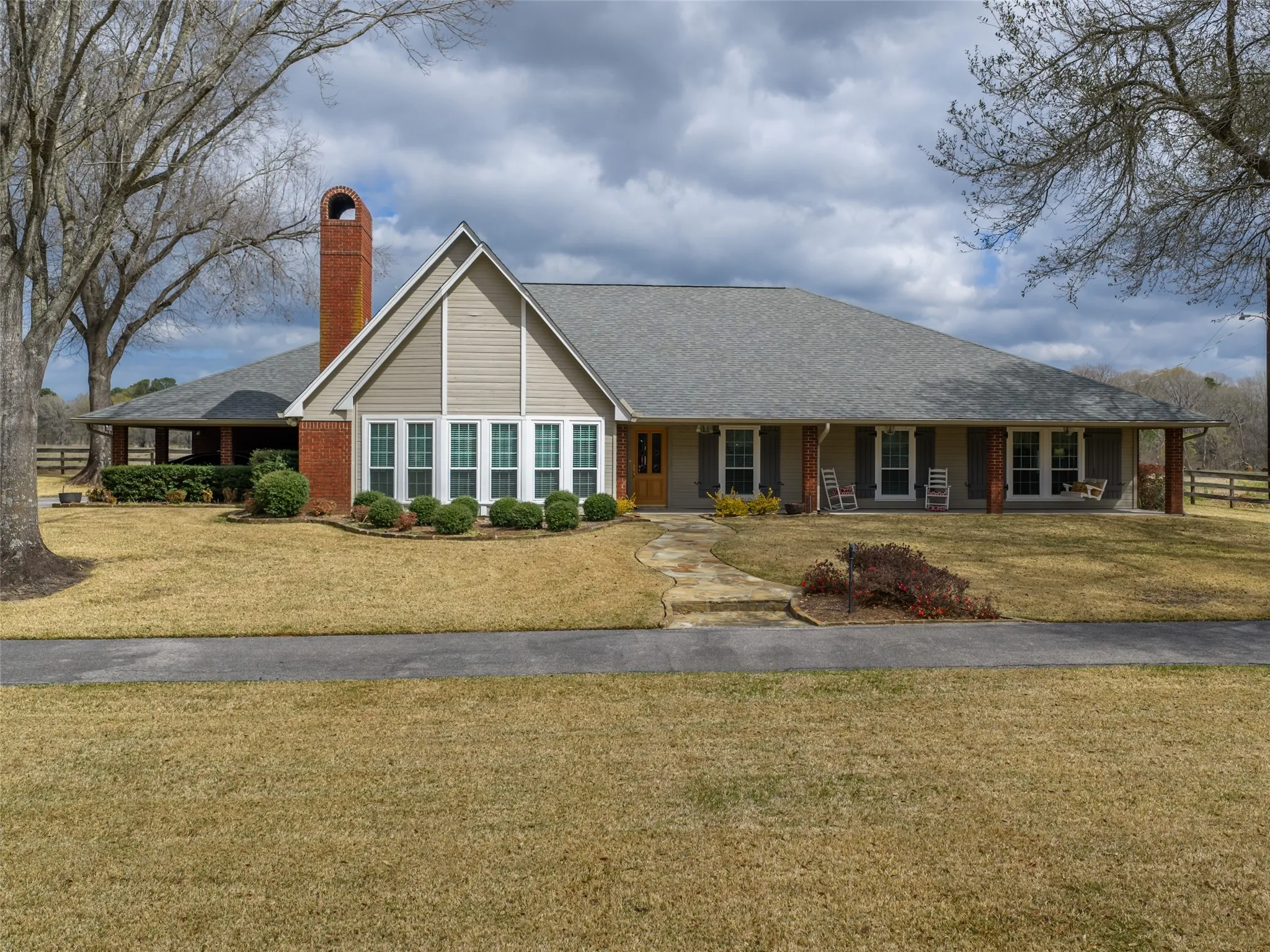 Brick and siding exterior with a prominent brick chimney, multiple window configurations, a full-length covered porch, and a stone pathway leading to the main entry