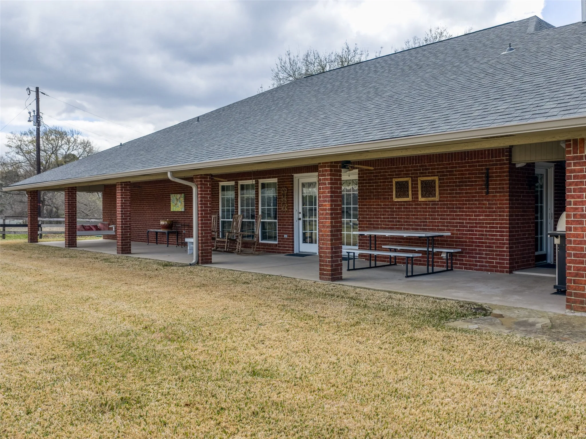 Brick exterior with an extended covered patio, multiple windows, and a shingled roof