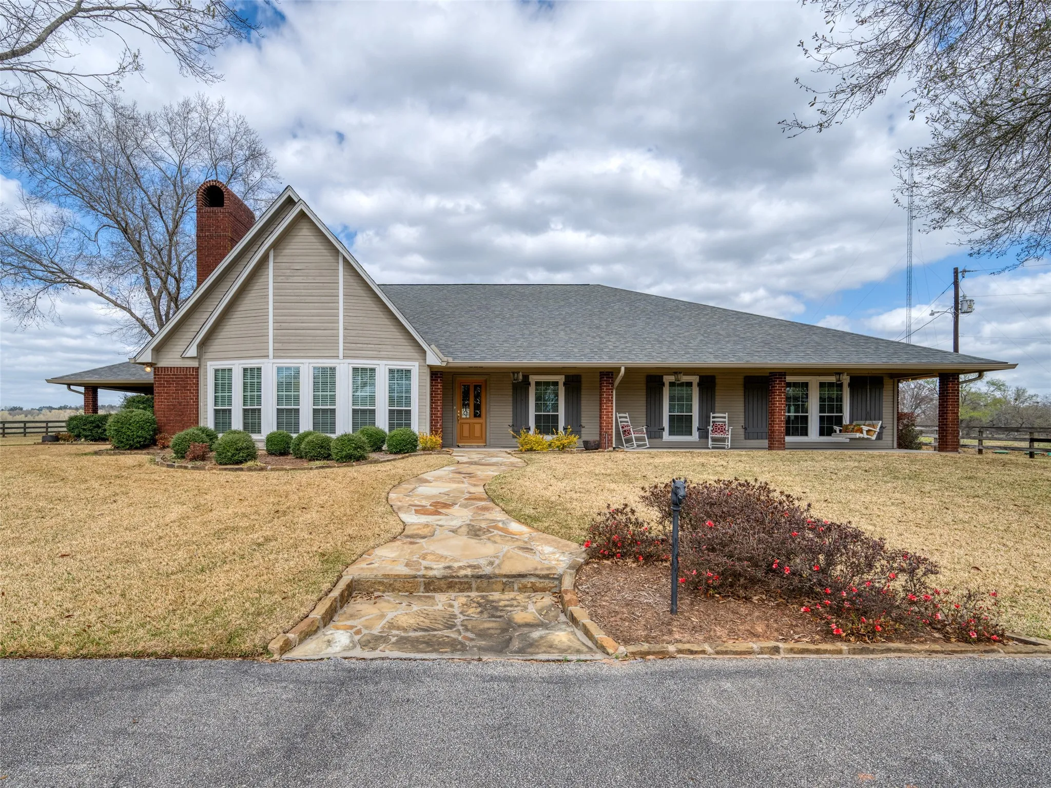 Expansive single-story residence with a prominent gabled roofline, a lengthy covered front porch supported by brick columns, a stone-finish walkway, and a brick chimney