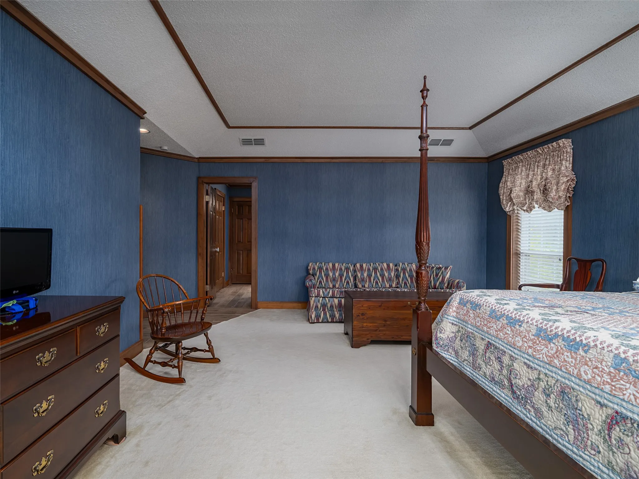 Tray ceiling with wood trim, textured blue wall covering, and light-toned carpeting