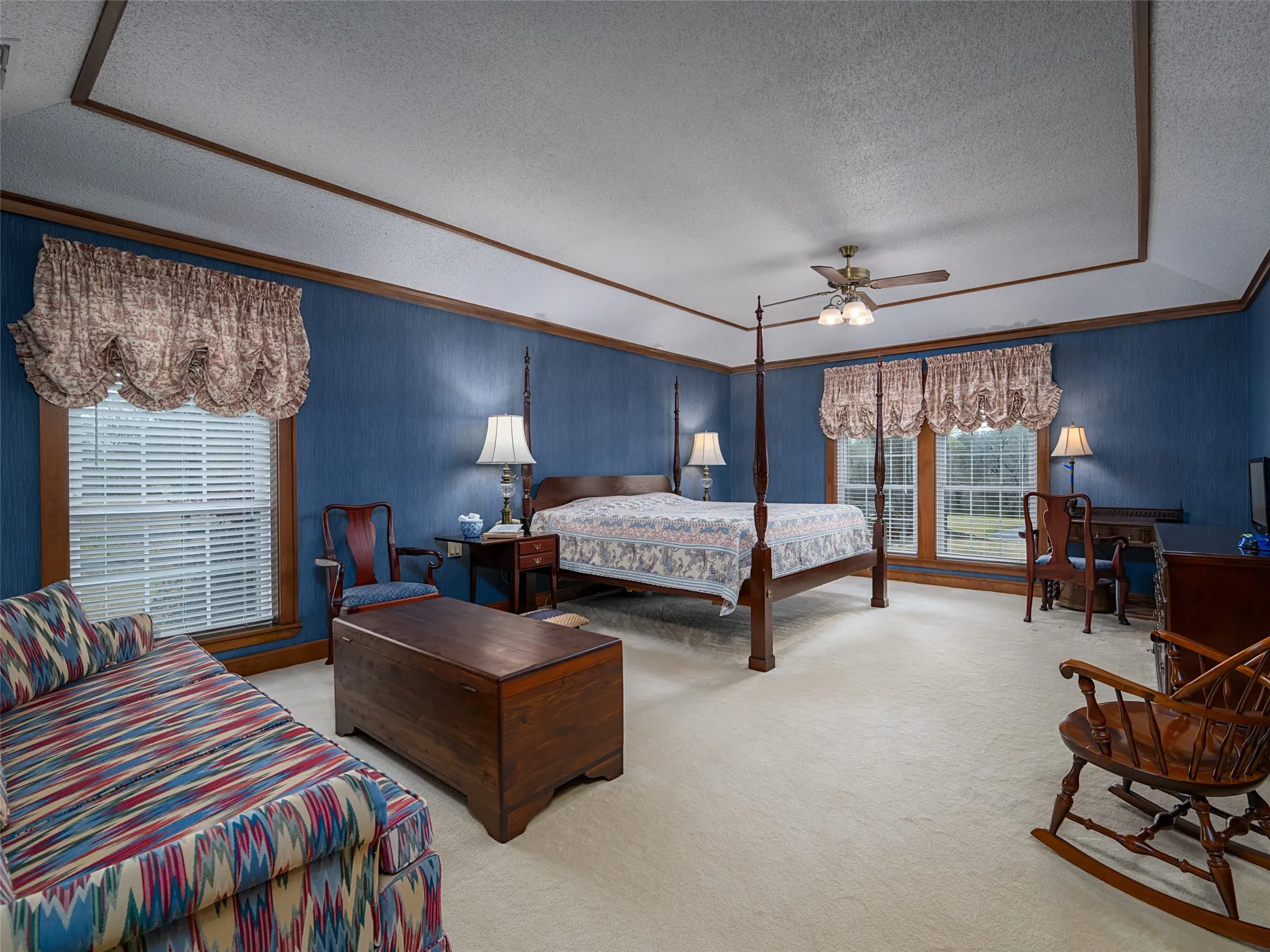 Tray ceiling with wood trim, ceiling fan light fixture, multiple windows with blinds, and blue textured wall covering