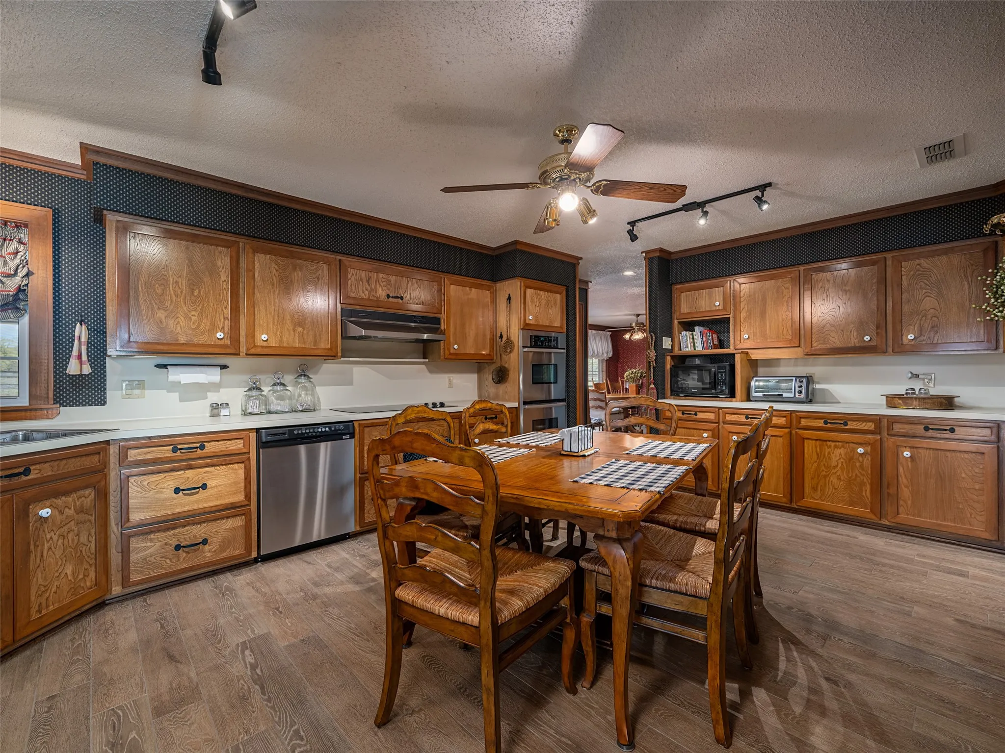 Wood-finish flooring, ample wood cabinetry, light-toned countertops, stainless steel appliances, and a ceiling fan with integrated lighting