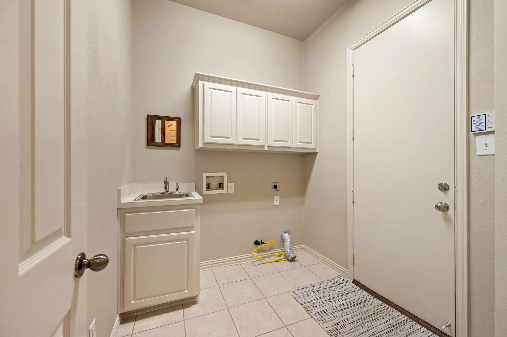 Utility room with tiled flooring, built-in cabinetry, an integrated sink, and interior door access