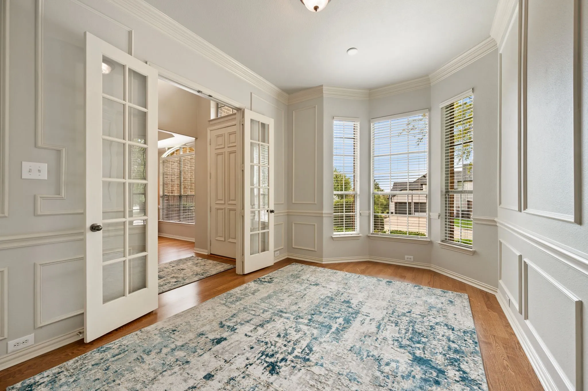 Hardwood-style flooring, wainscoting and crown molding, bay window with blinds, and French doors