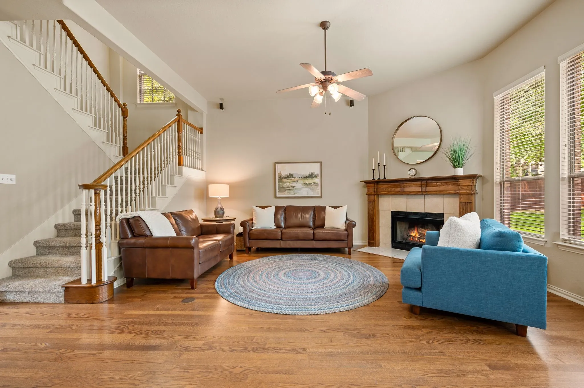 Vaulted ceiling with a ceiling fan, hardwood flooring, corner fireplace with a wood mantel and tile surround, and large windows with blinds