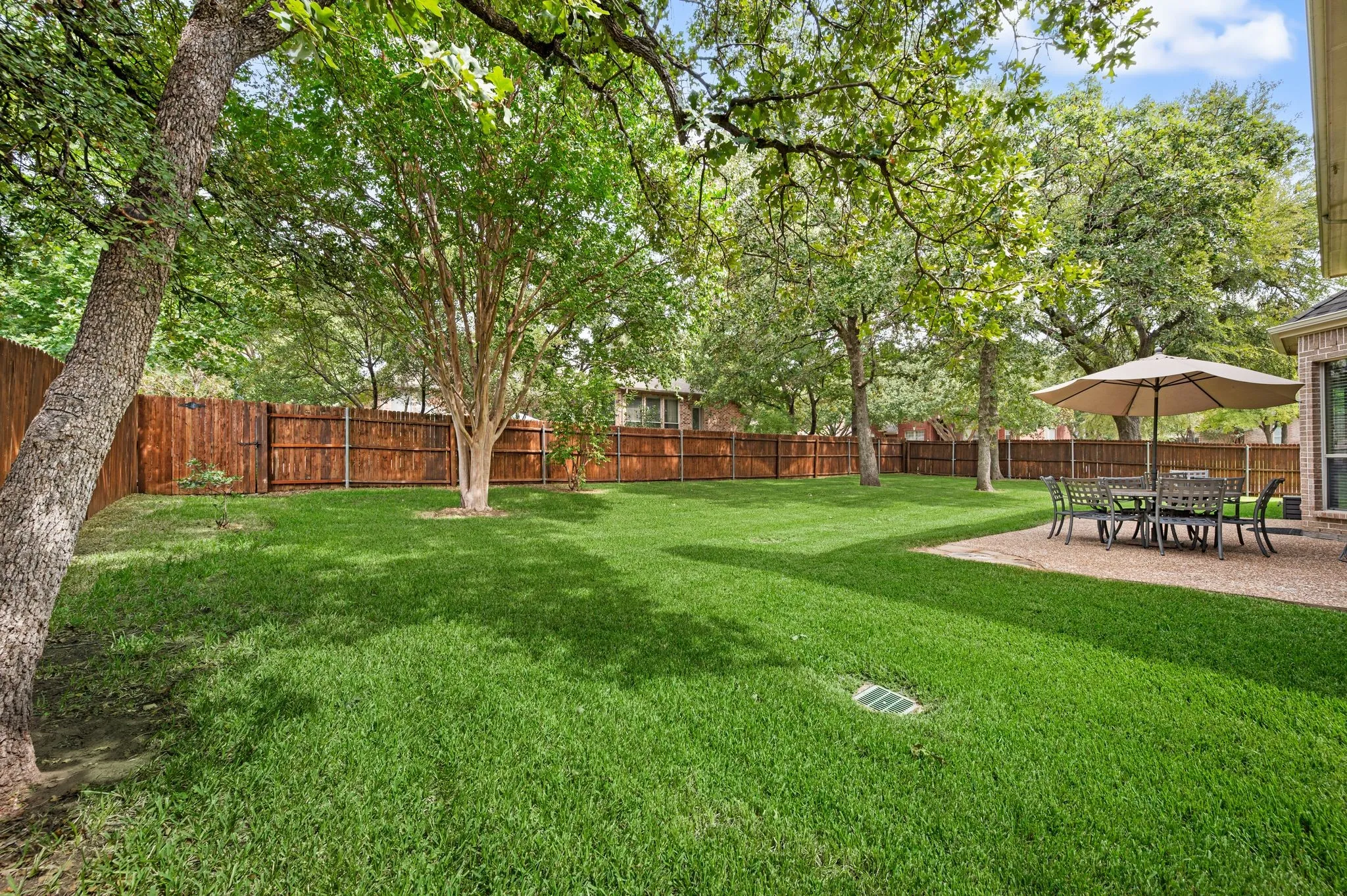 Expansive green lawn, mature trees, wood privacy fencing, and a paved patio area