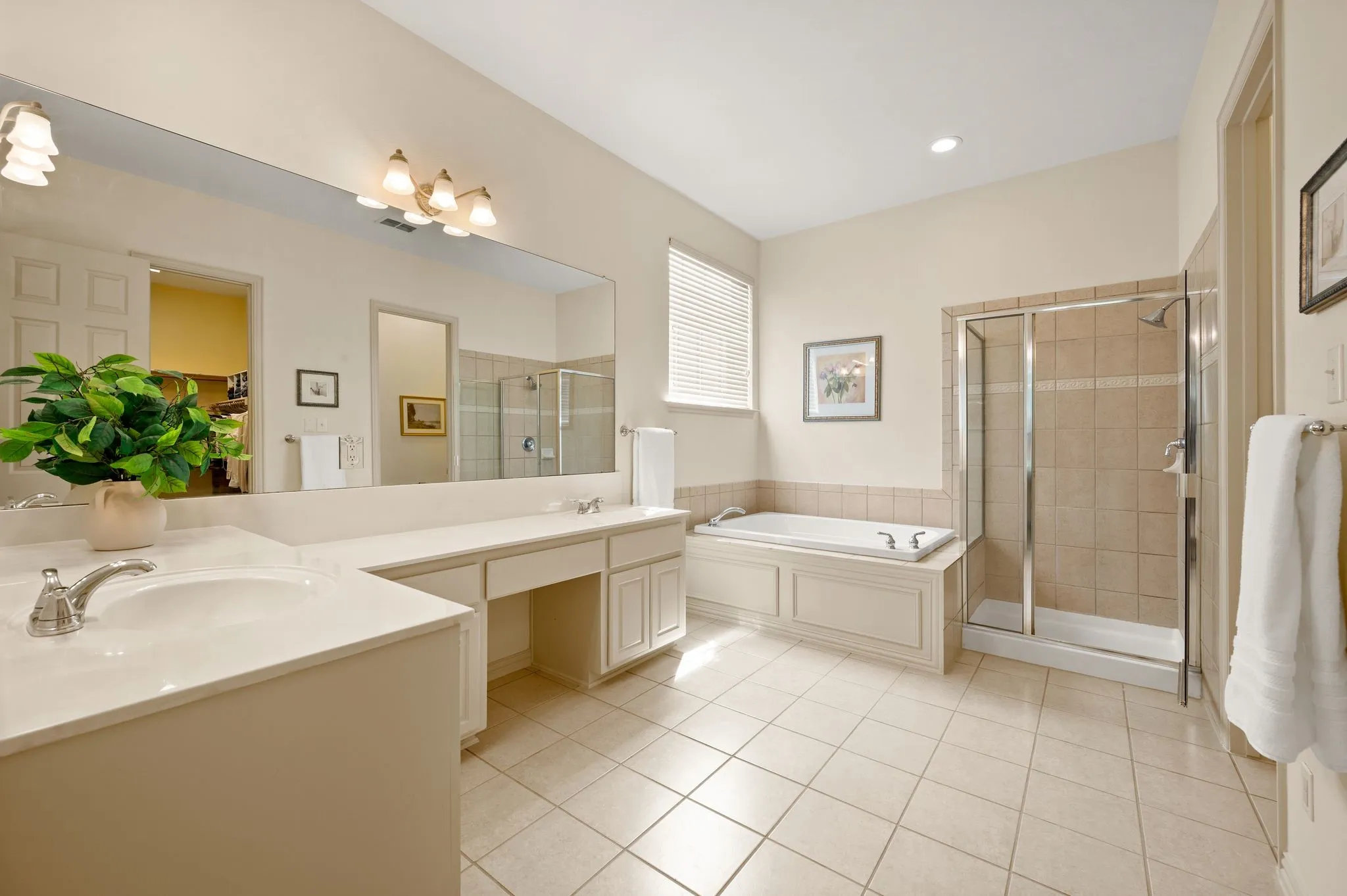 Dual vanity with integrated sinks, expansive mirror, separate shower enclosure with tile surround, built-in bathtub, and tiled flooring