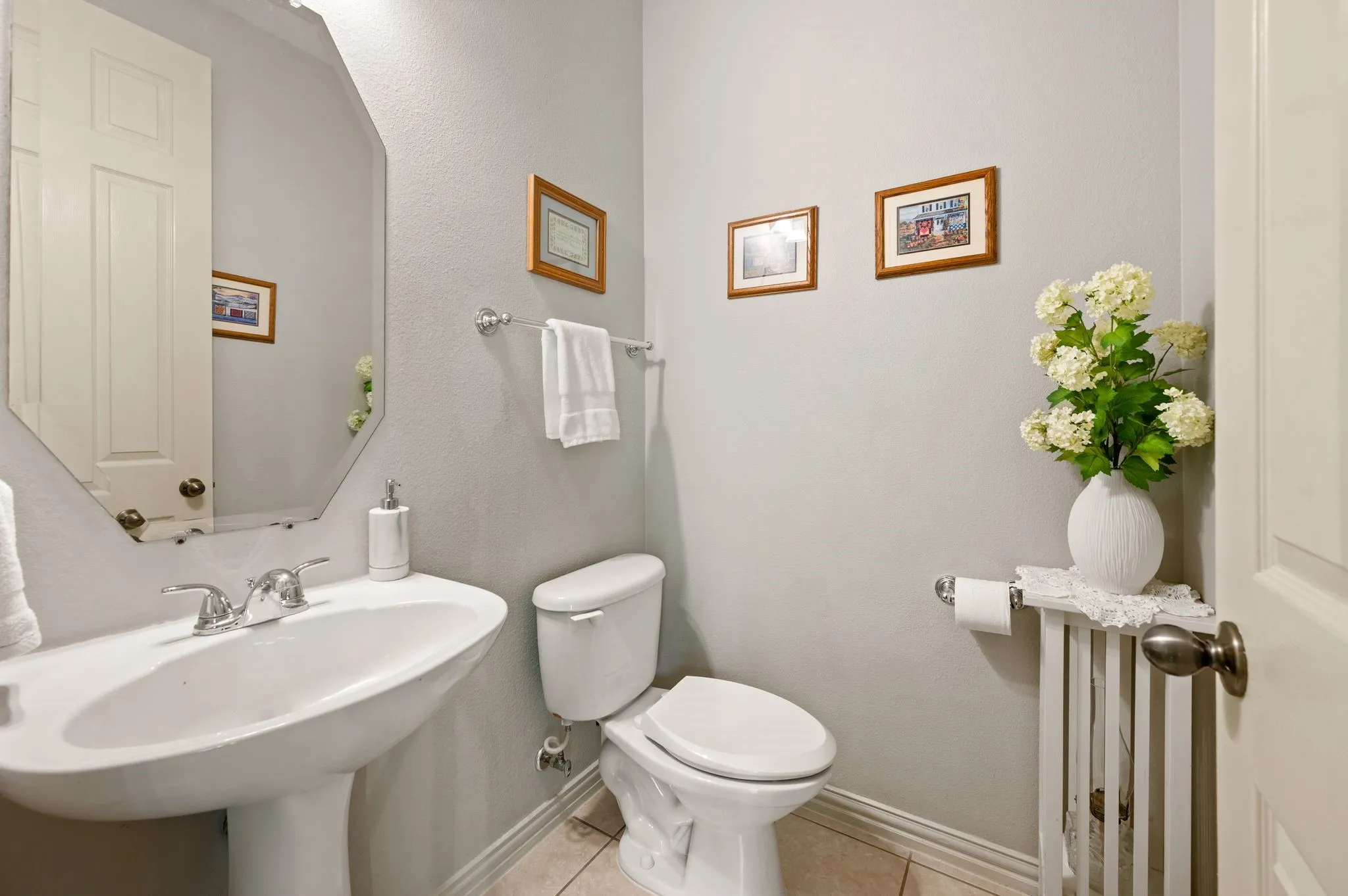 Pedestal sink with chrome faucet, octagonal mirror, ceramic toilet, and tile flooring