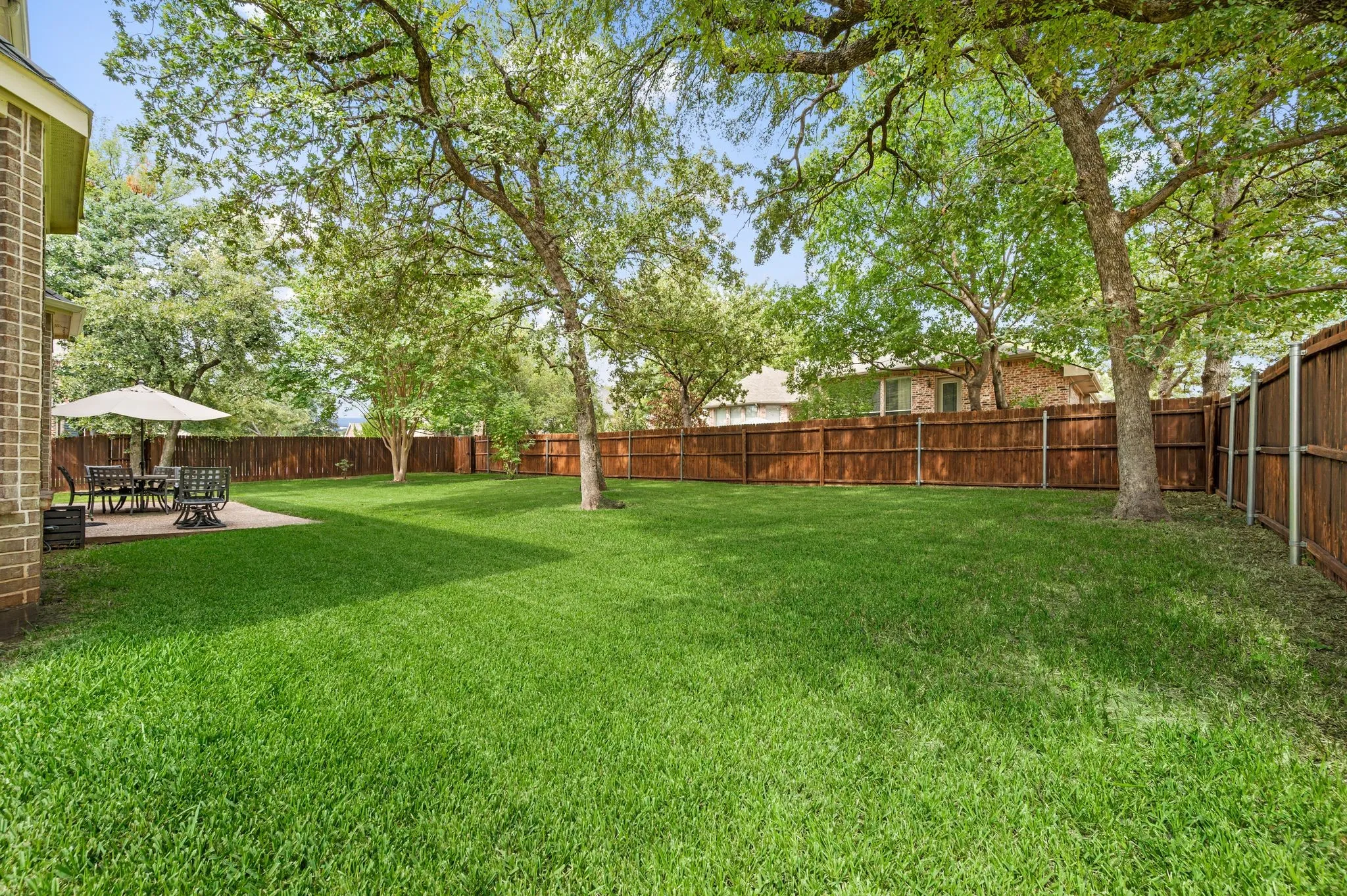 Expansive green lawn with mature trees and a privacy fence