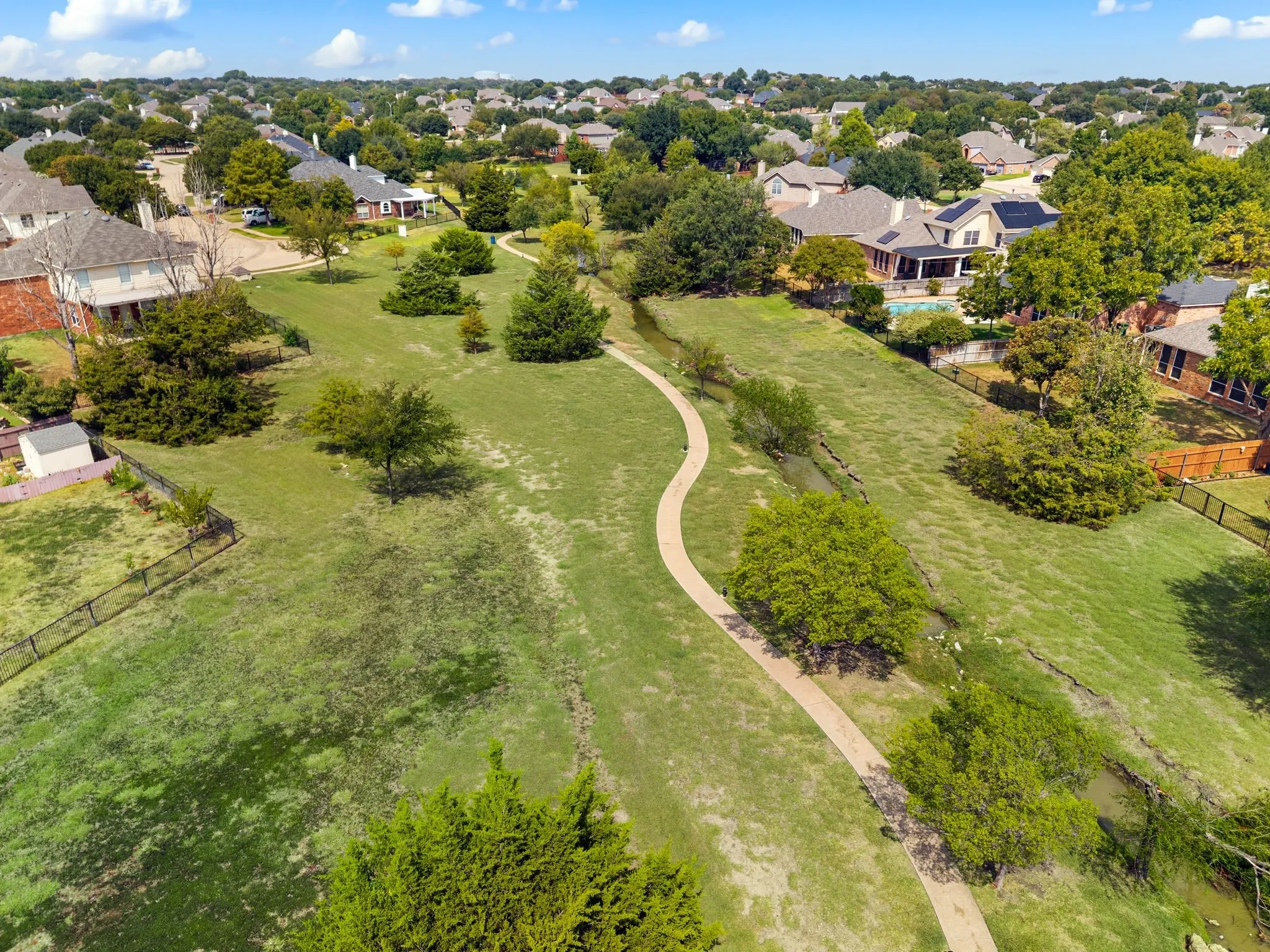 Expansive green spaces with a winding pathway, mature trees, and residential surroundings