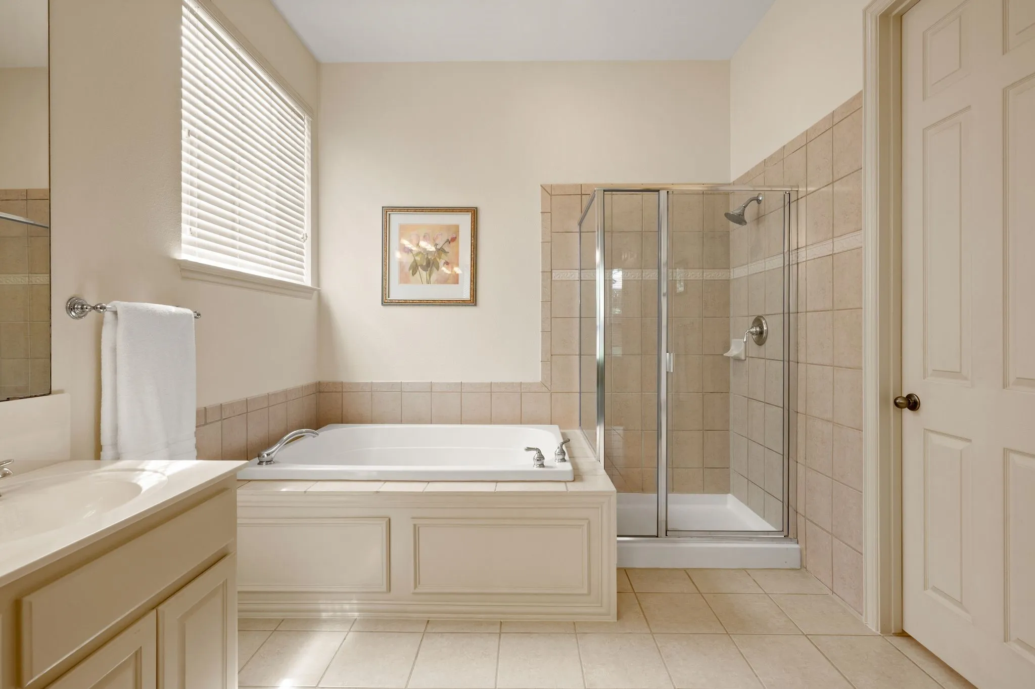 Built-in soaking tub, separate glass-enclosed shower, single vanity with integrated sink, panel-style cabinetry, and tile flooring