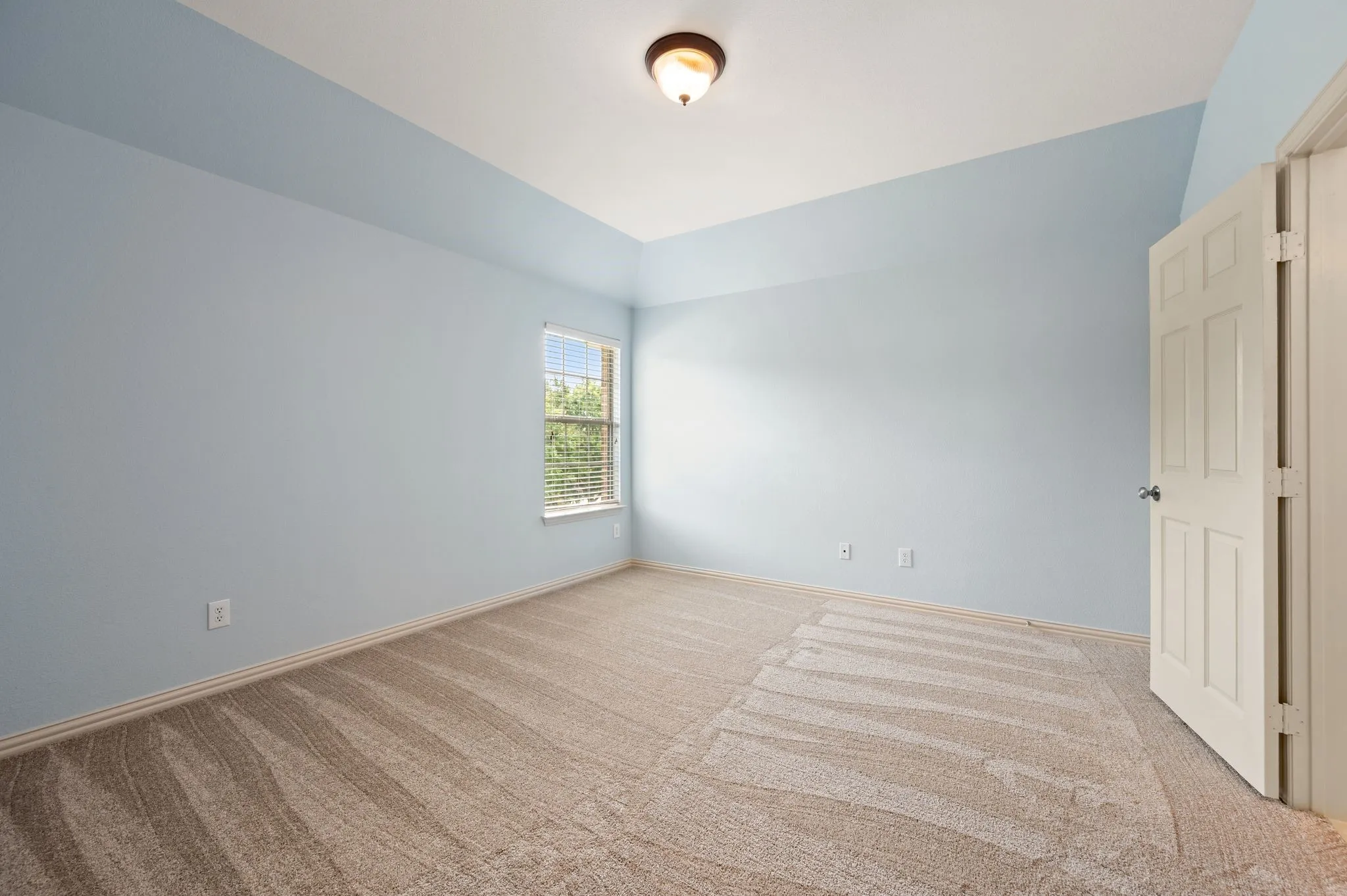 Vaulted ceiling, wall-to-wall carpeting, single window with blinds, paneled door, flush mount ceiling light fixture