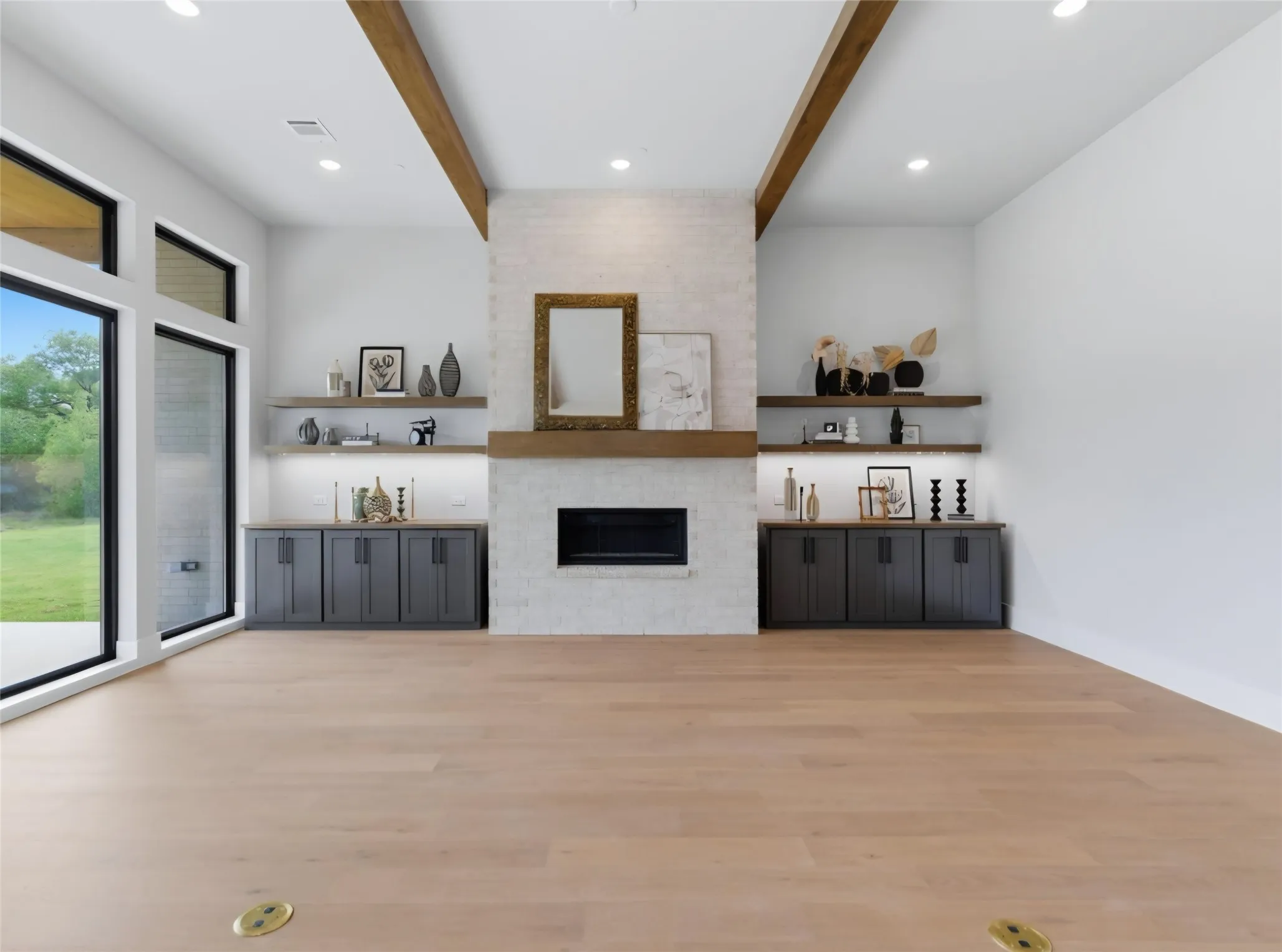 Expansive living area featuring light wood-finish flooring, a white brick fireplace with a wood mantel, built-in cabinetry, and large windows