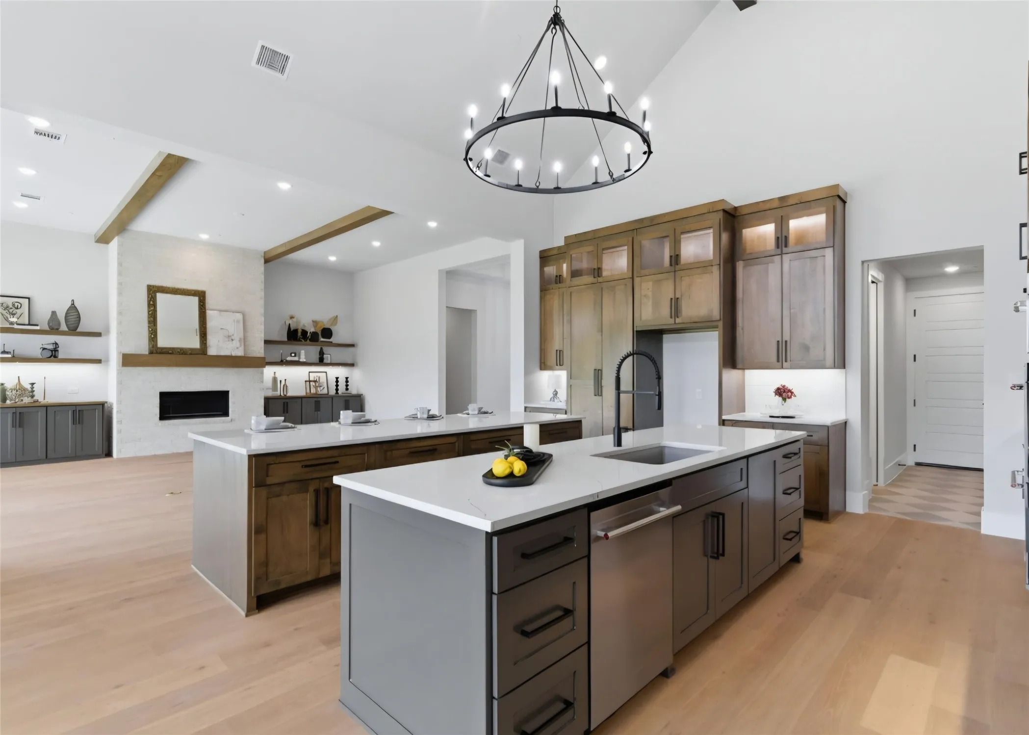 Vaulted ceiling with exposed wood beams, dual kitchen islands with light countertops, built-in electric fireplace, and wood-finish flooring