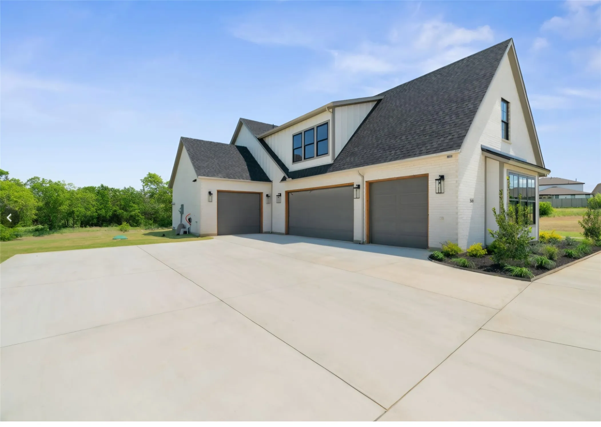 Three-car garage with gray doors, white brick exterior, dark roof, accent windows, and landscaped beds