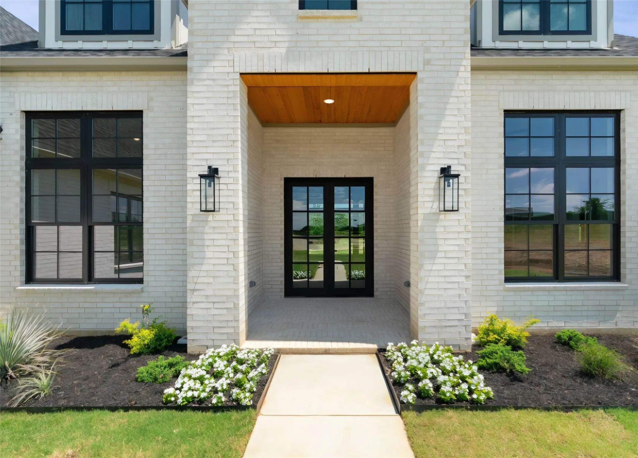 White brick exterior featuring a recessed entry, wood-finish ceiling, double glass-paneled doors, and black grid-pattern windows