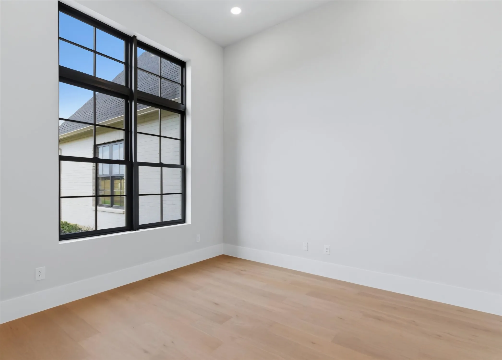 Expansive window with black grid panes, recessed ceiling lighting, light wood-finish flooring, and crisp white walls