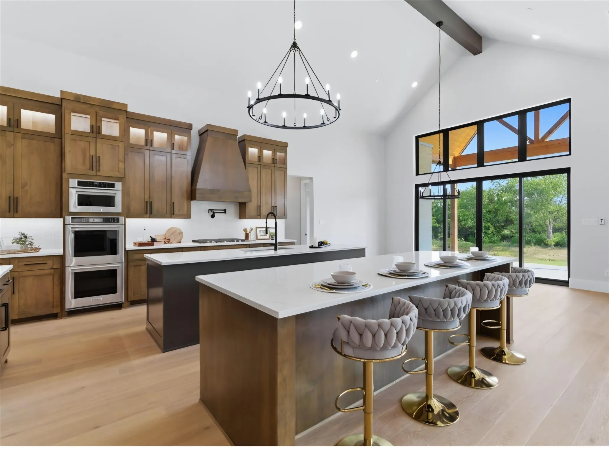 Vaulted ceiling with an exposed beam, light wood-finish flooring, full-height cabinetry with integrated appliances, kitchen island with a white countertop, and expansive glass doors