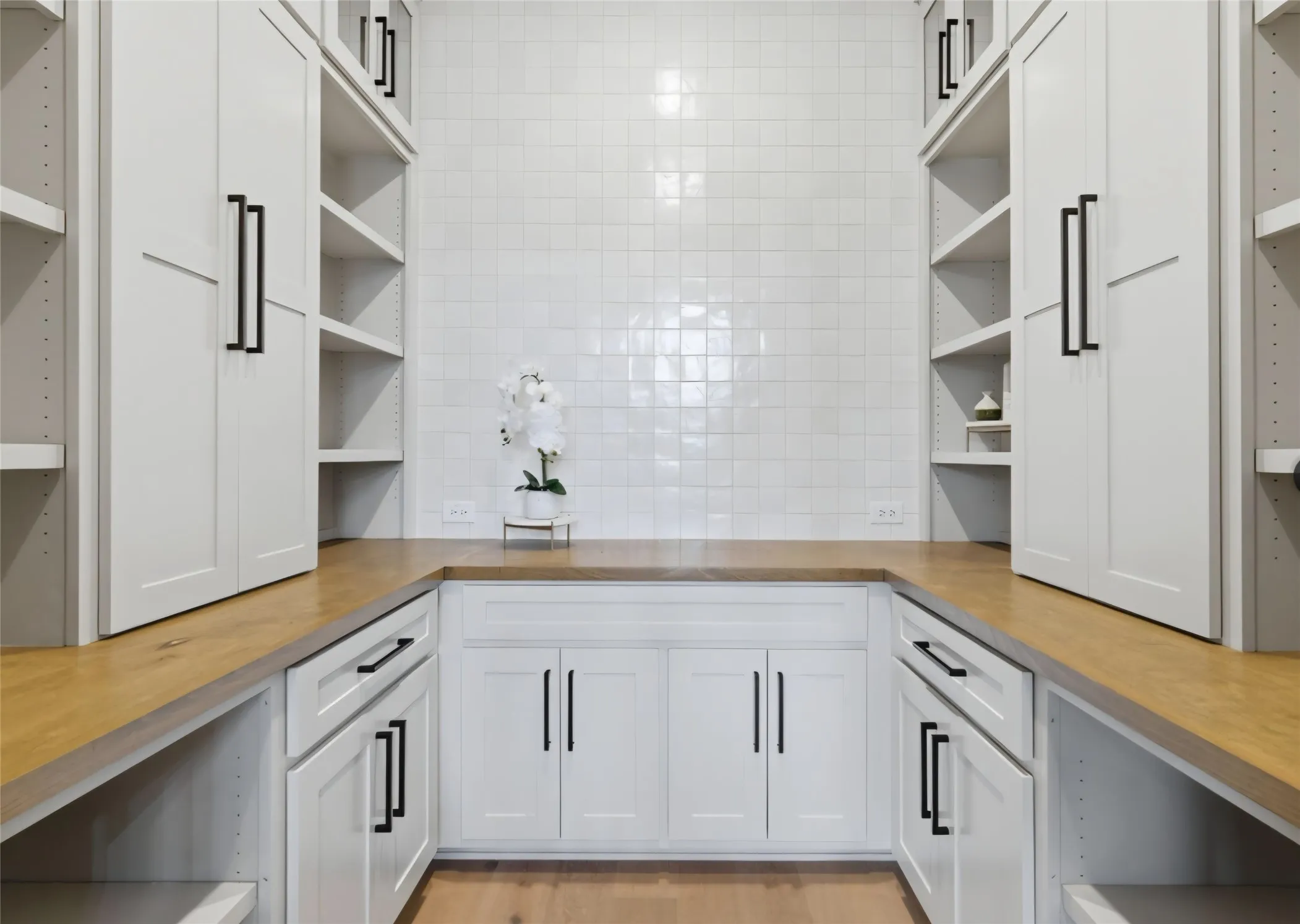 White cabinetry with black hardware, wood-finish countertops, and square tile backsplash