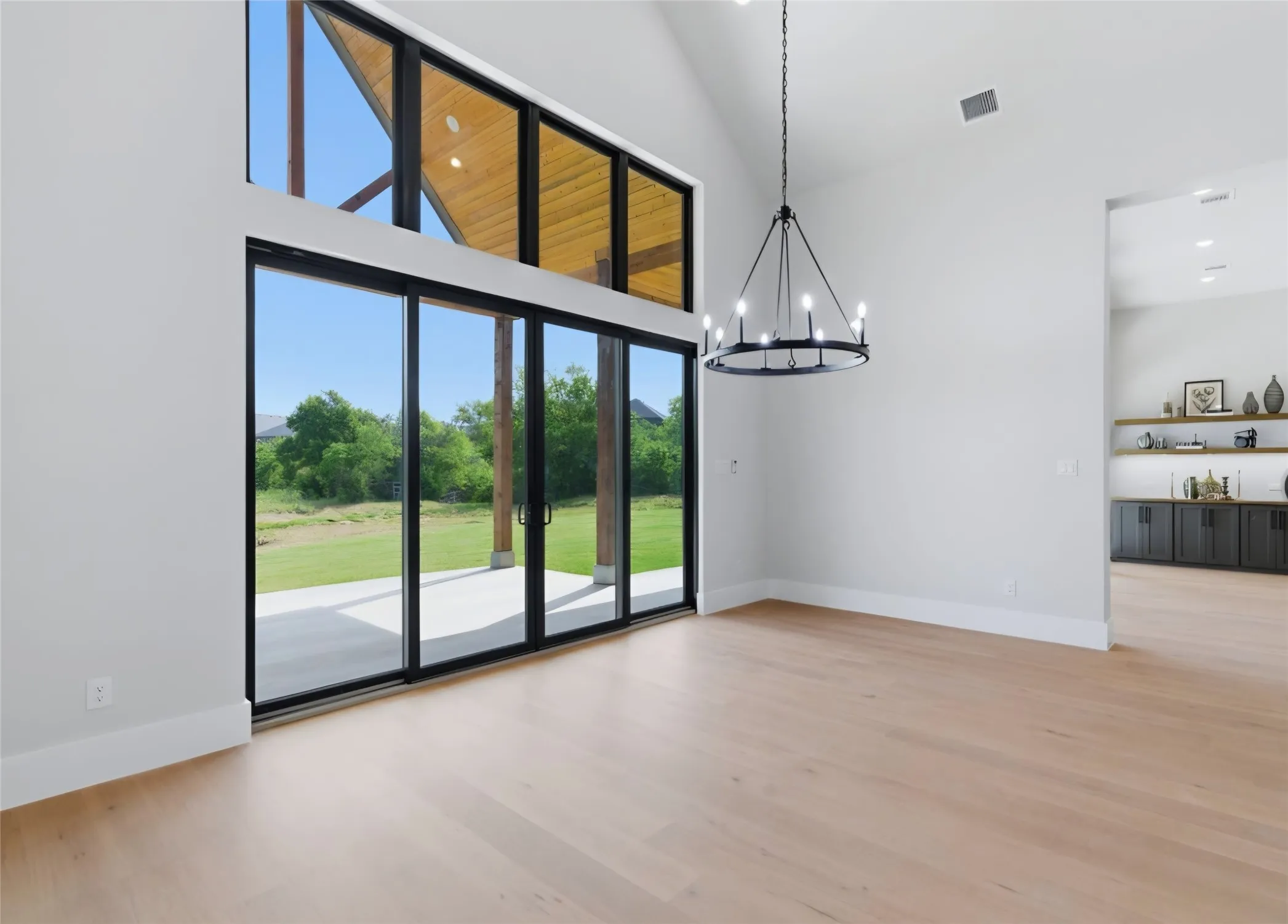 Vaulted ceiling with wood-finish accents, large sliding glass doors, light wood-finish flooring, contemporary chandelier, and built-in shelving with lower cabinetry