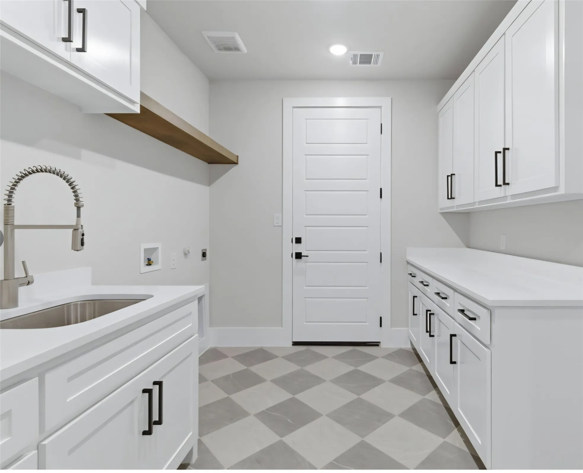 White cabinetry with black hardware, stone-finish countertops, stainless steel sink with pull-down faucet, wood-finish floating shelf, and patterned floor tiling