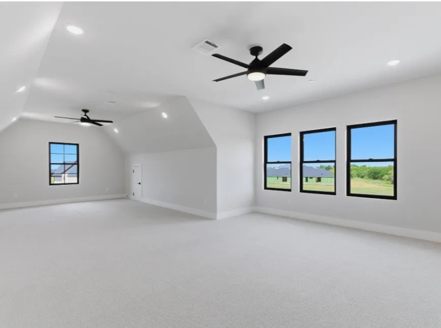 Expansive room featuring vaulted ceilings, recessed lighting, ceiling fans, multiple windows with dark frames, and light-toned carpeting
