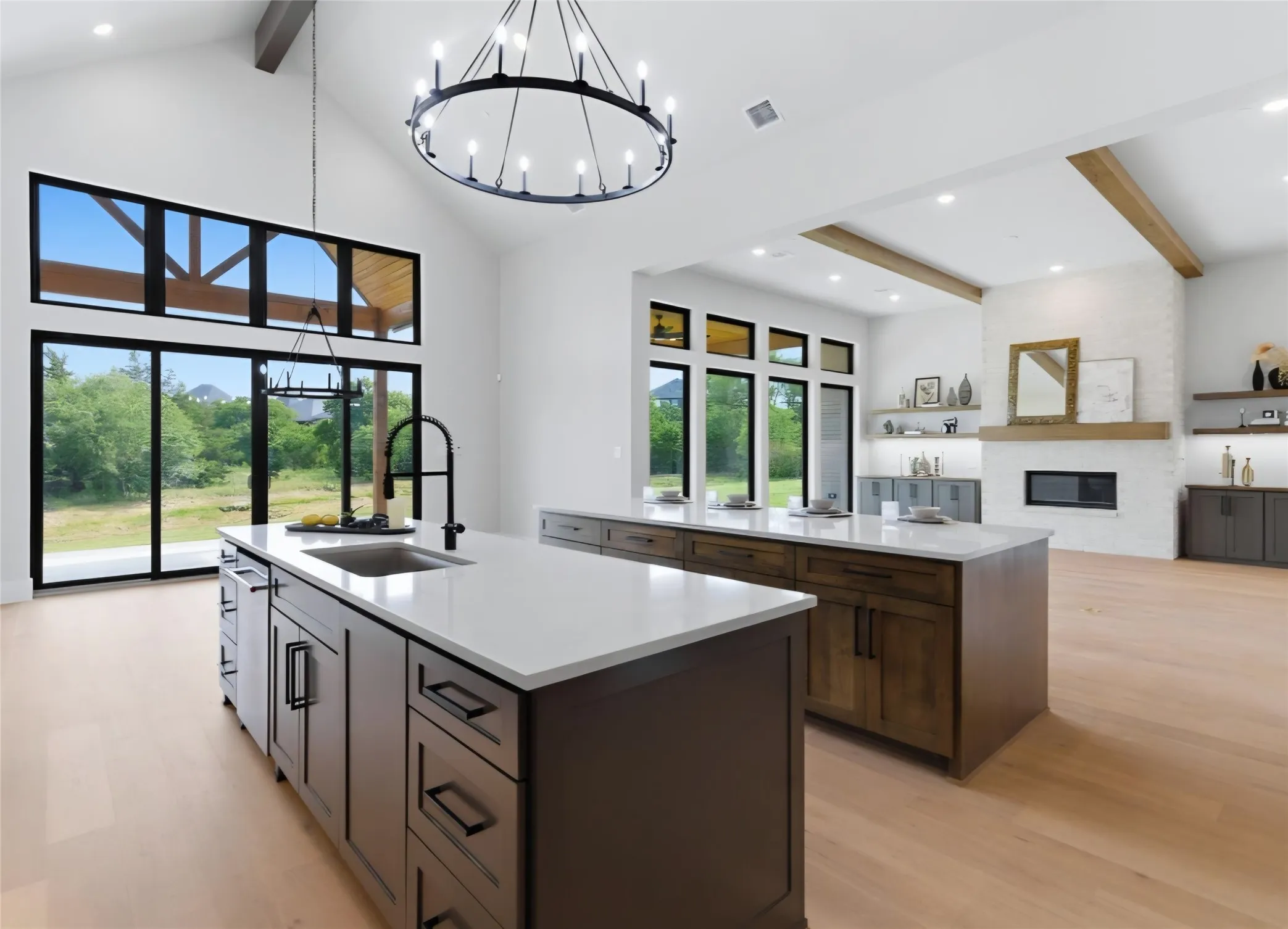 Vaulted ceilings with exposed beams, multiple kitchen islands with white countertops and dark cabinetry, wood-finish flooring, and a fireplace with a white brick surround and wood mantel