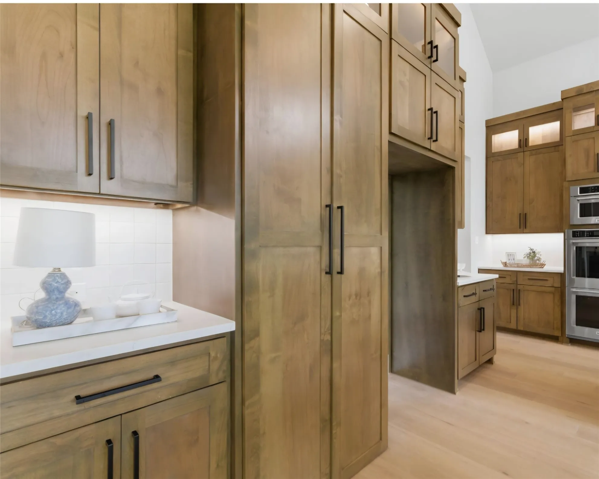 Wood-finish cabinetry with black hardware, light wood-finish flooring, white countertops, white subway tile backsplash, and built-in stainless steel appliances