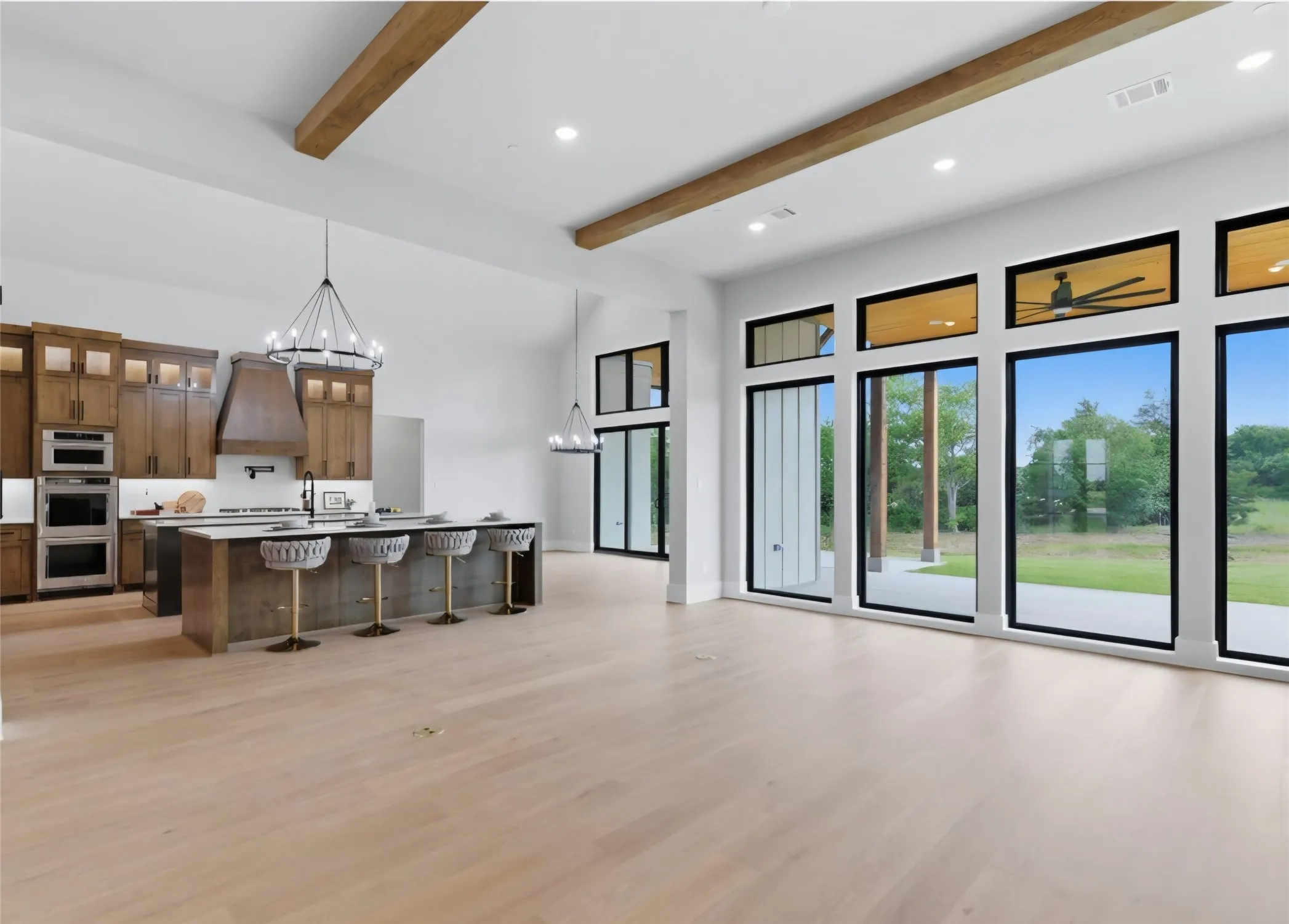 Expansive open-concept living space with wood-finish flooring, exposed ceiling beams, and a modern kitchen featuring wood cabinetry