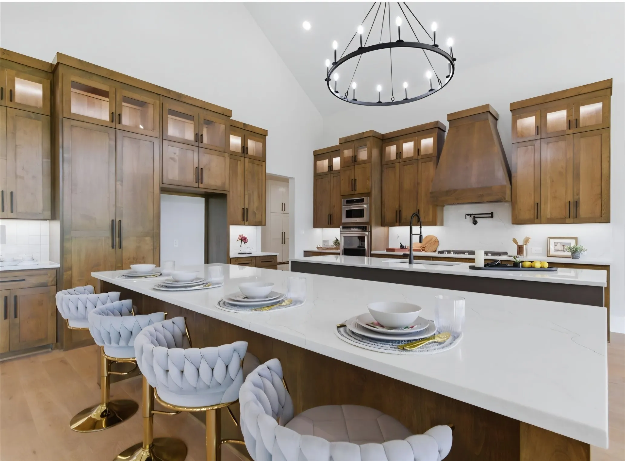 Vaulted ceiling with a large circular chandelier, wood-finish cabinetry, built-in double ovens, white countertops, and wood-finish flooring