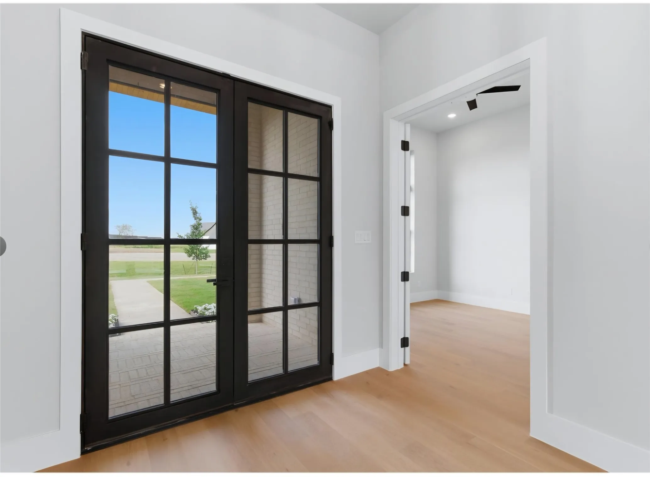 Black-framed double glass doors, wood-finish flooring, white walls, and recessed lighting