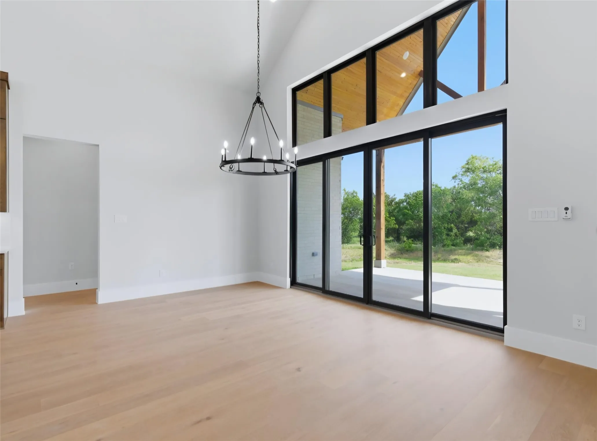Vaulted ceiling with wood paneling, wood-finish flooring, black chandelier, and multi-panel sliding glass doors