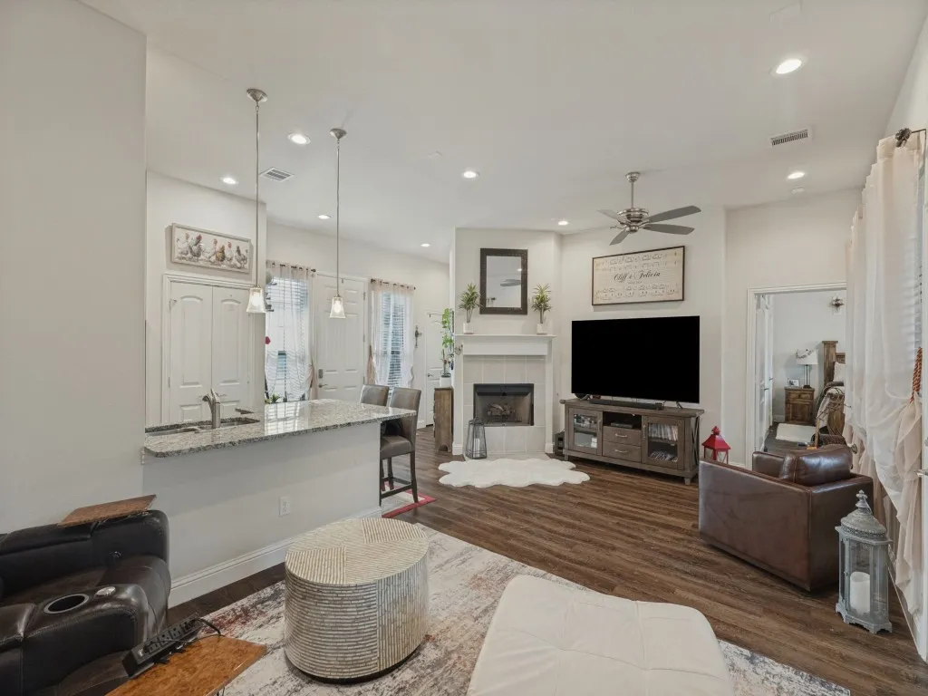 Recessed lighting, wood-finish flooring, granite countertop peninsula, fireplace with mantel, and ceiling fan