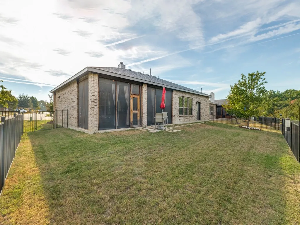 Expansive backyard featuring a manicured lawn, brick exterior, and a screened-in porch with an exterior door