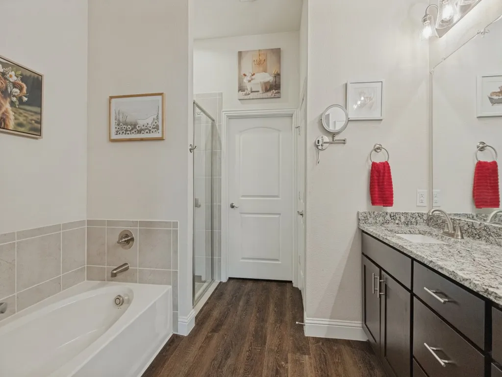 Bathroom featuring a built-in tub, separate shower enclosure, wood-finish flooring, and a vanity with a stone countertop