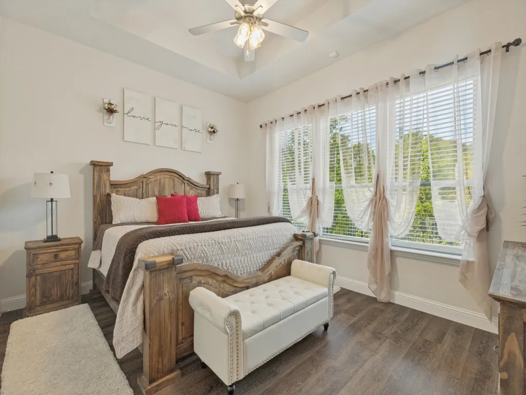 Tray ceiling with a ceiling fan, multiple large windows, and wood-finish flooring