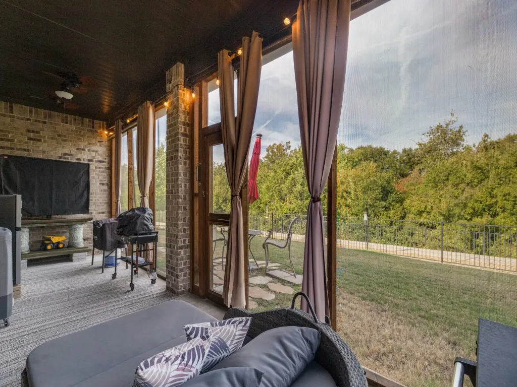 Screened-in porch featuring brick accent walls, exposed wood beam ceiling, ceiling fan, and multiple glass-paneled doors with direct outdoor access