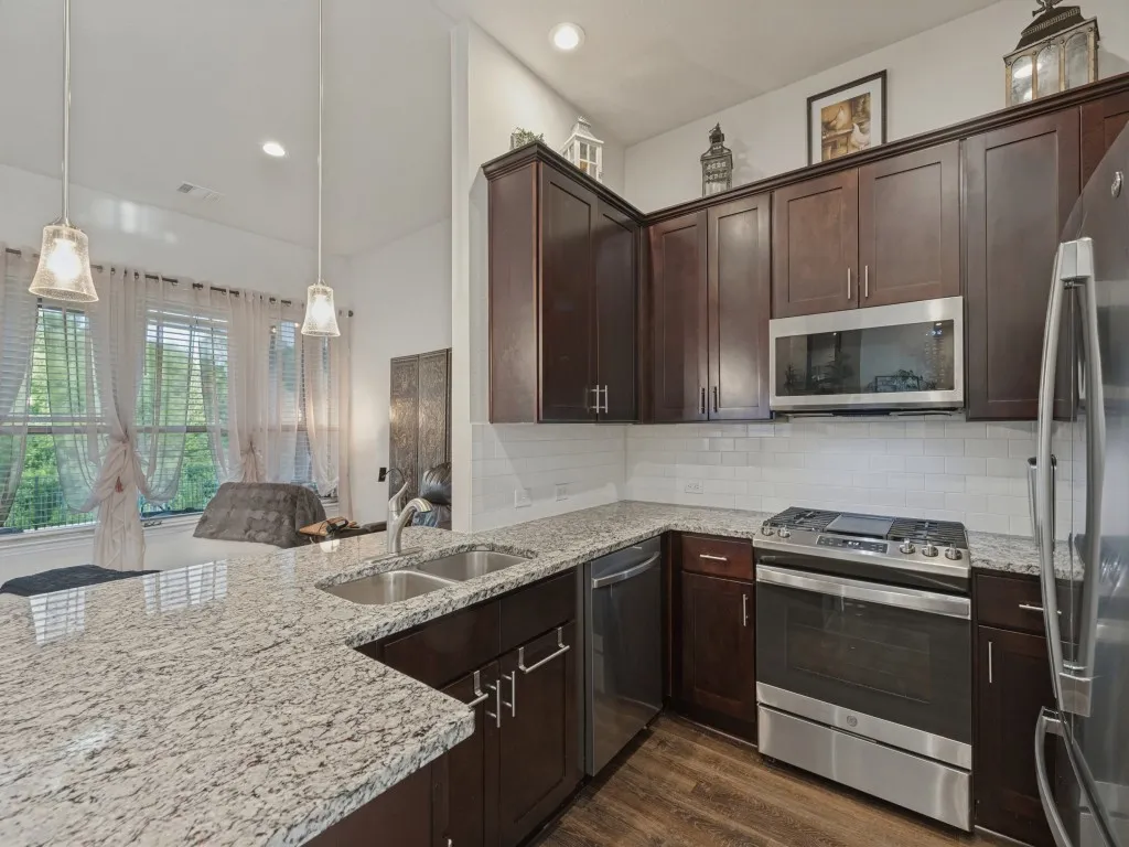 Kitchen featuring granite countertops, wood-finish flooring, stainless steel appliances, dark wood-finish cabinetry, and a subway tile backsplash