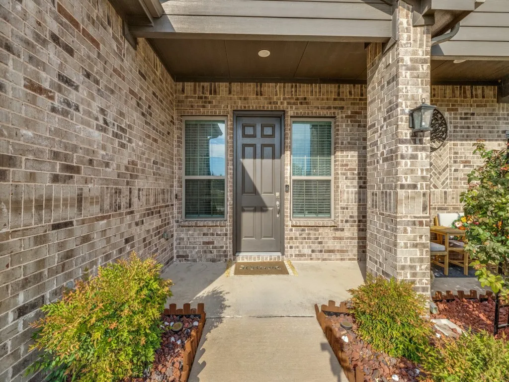 Brick exterior with a covered entry, dark paneled front door, and symmetrical windows with blinds