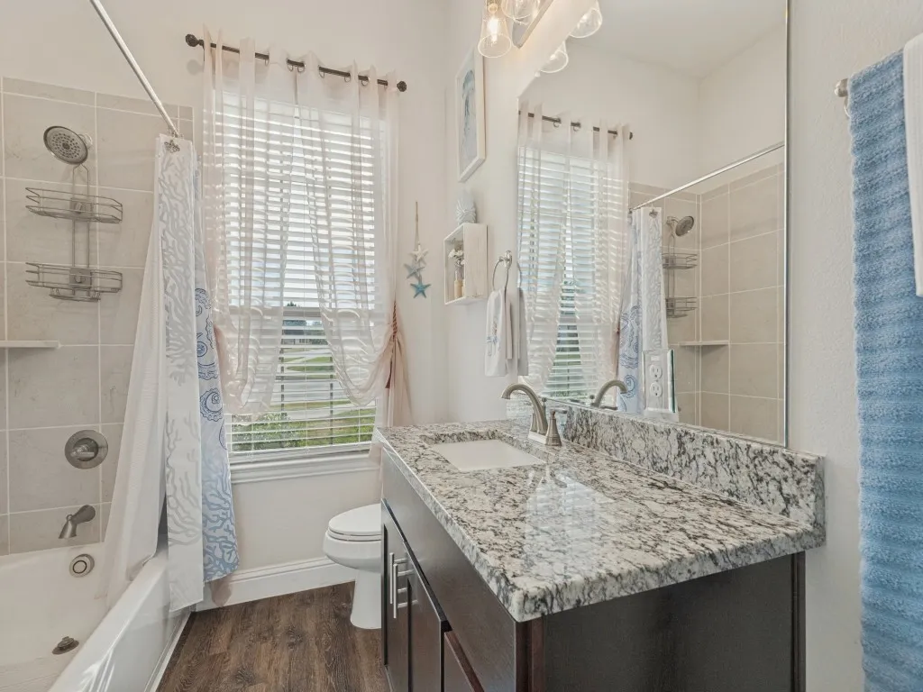 Wood-finish flooring, a vanity with a white countertop, and a shower-tub combination with tiled walls