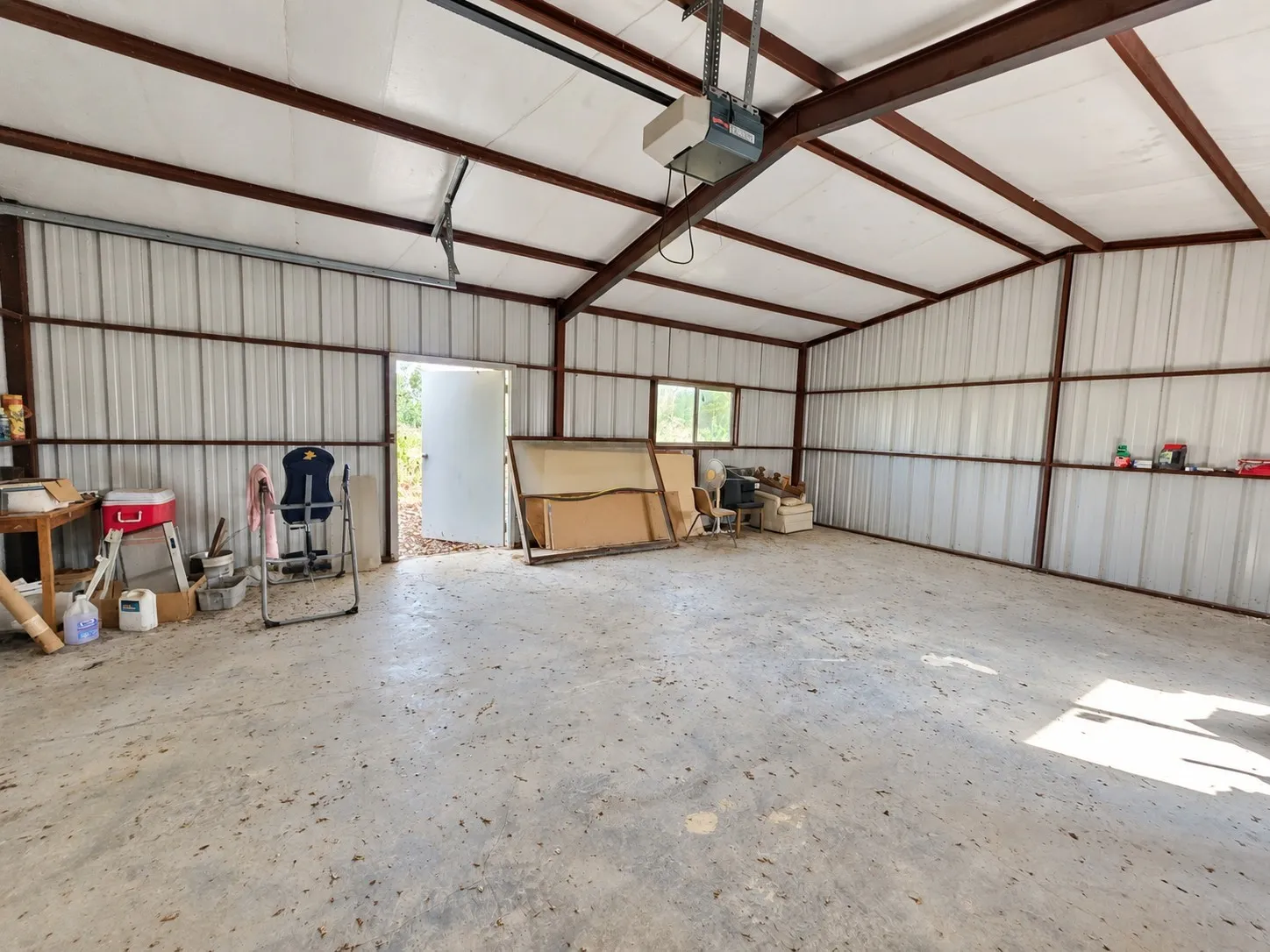 Spacious metal building with a concrete floor, exposed steel beam construction, corrugated metal walls, and a garage door opener