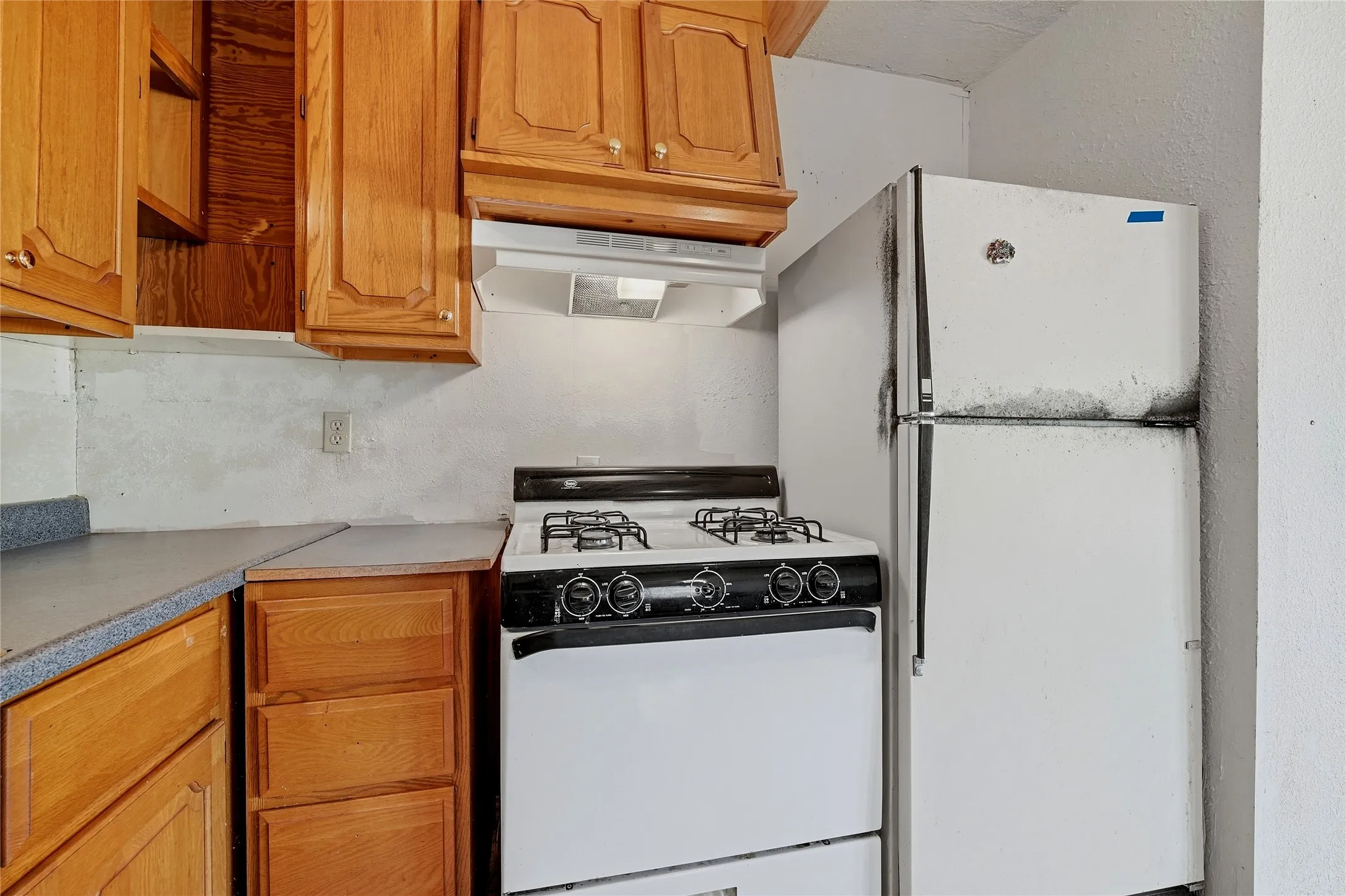 Wood-finish cabinetry and drawers, white range with four burners, white range hood, and a white refrigerator