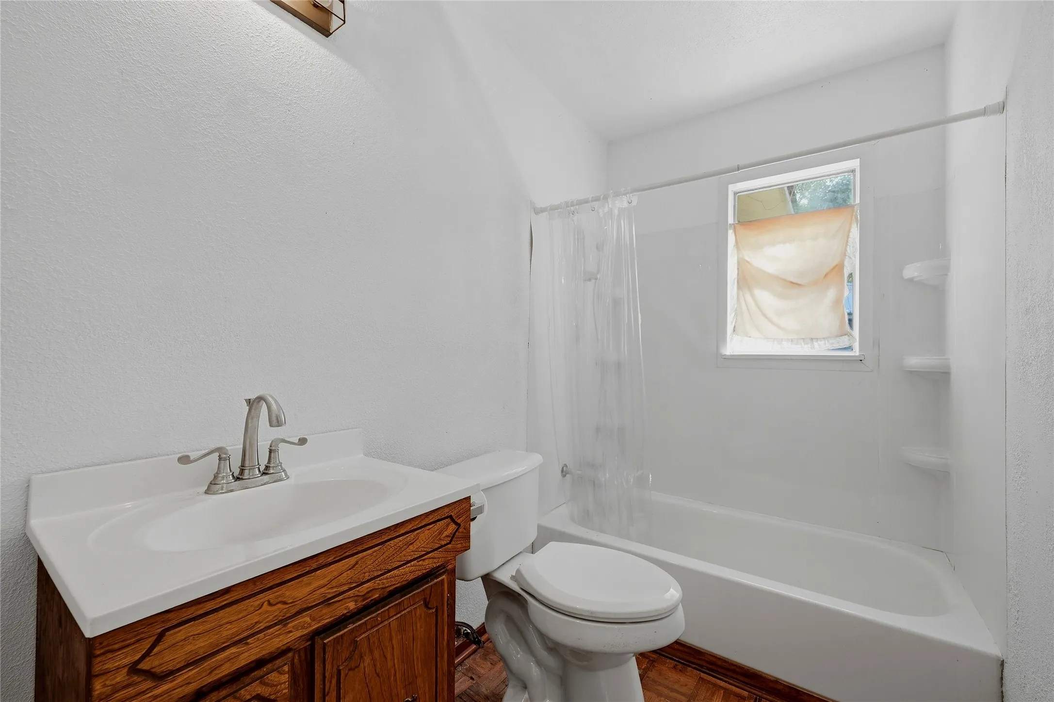 Tub and shower combination with an integrated soap dish, wood-finish flooring, and a vanity with a white countertop and integrated sink