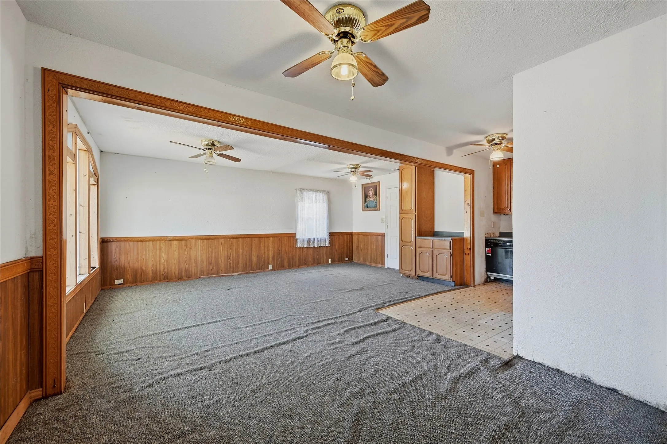 Expansive room featuring wood paneling, multiple ceiling fans, and an open doorway to a kitchen area with wood-finish cabinetry