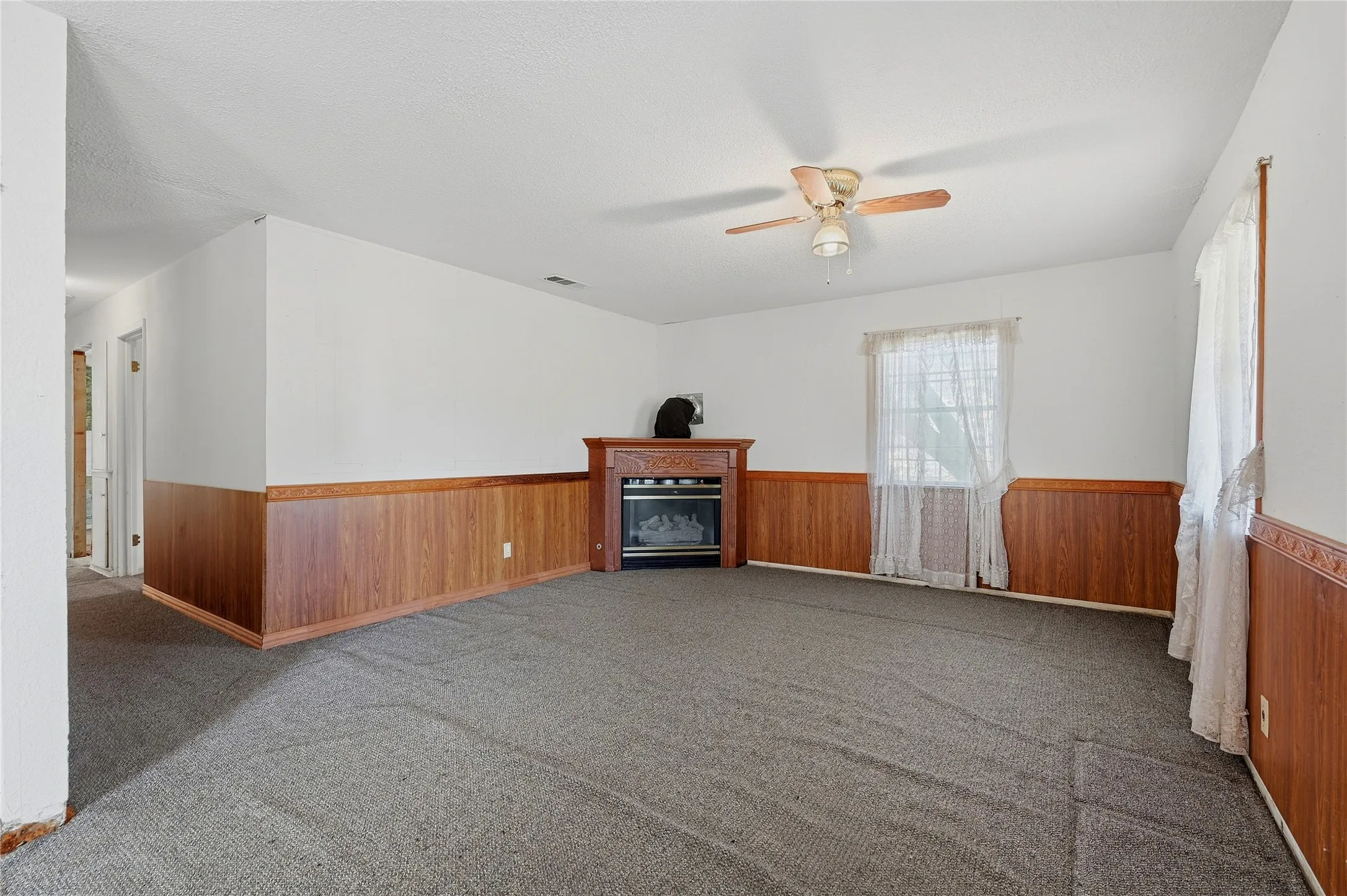 Spacious room featuring wood-finish wainscoting, a built-in fireplace, and a ceiling fan with light fixture