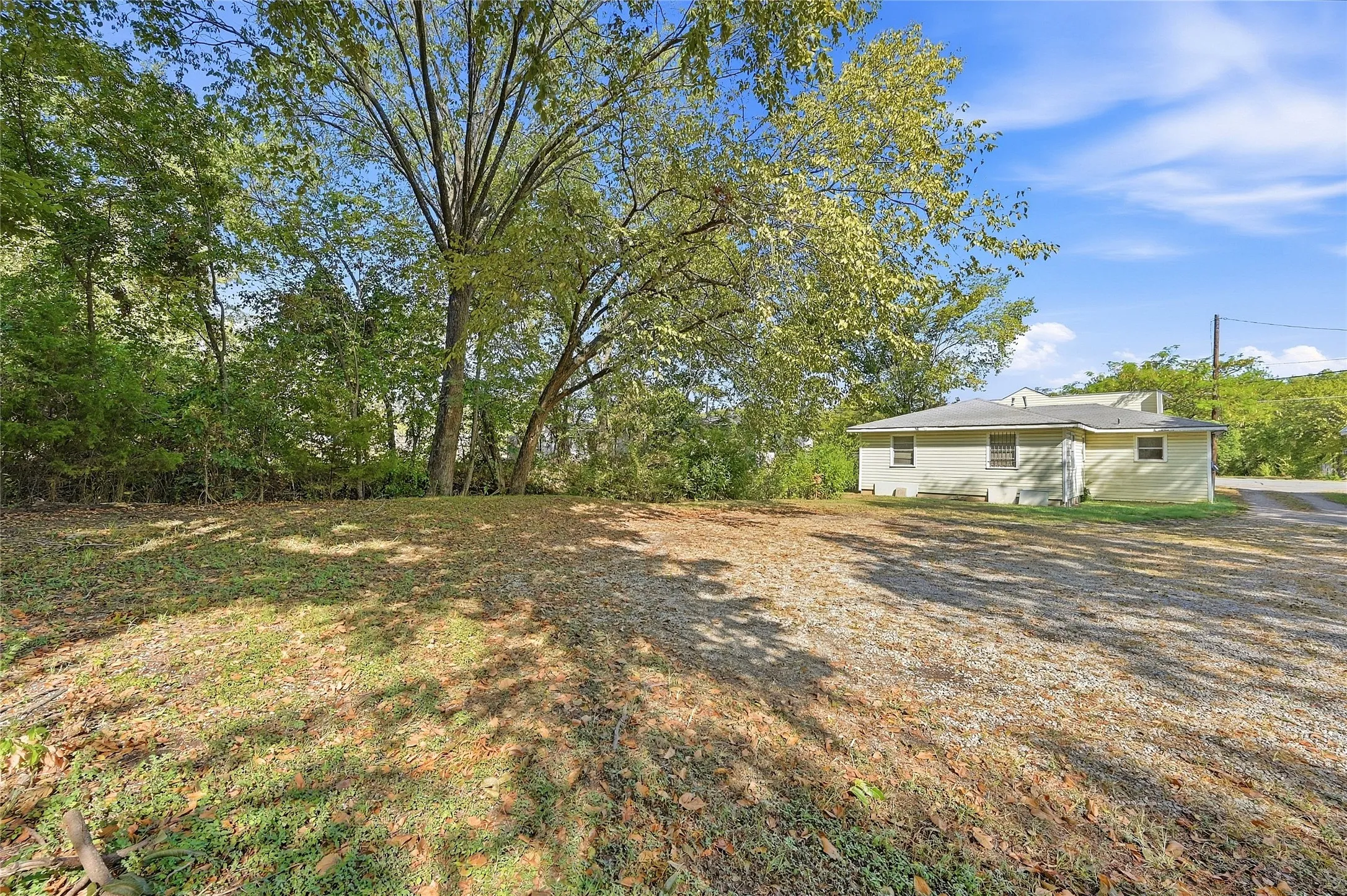 Expansive lot featuring a gravel surface, mature trees, and a single-story structure with a light-colored exterior